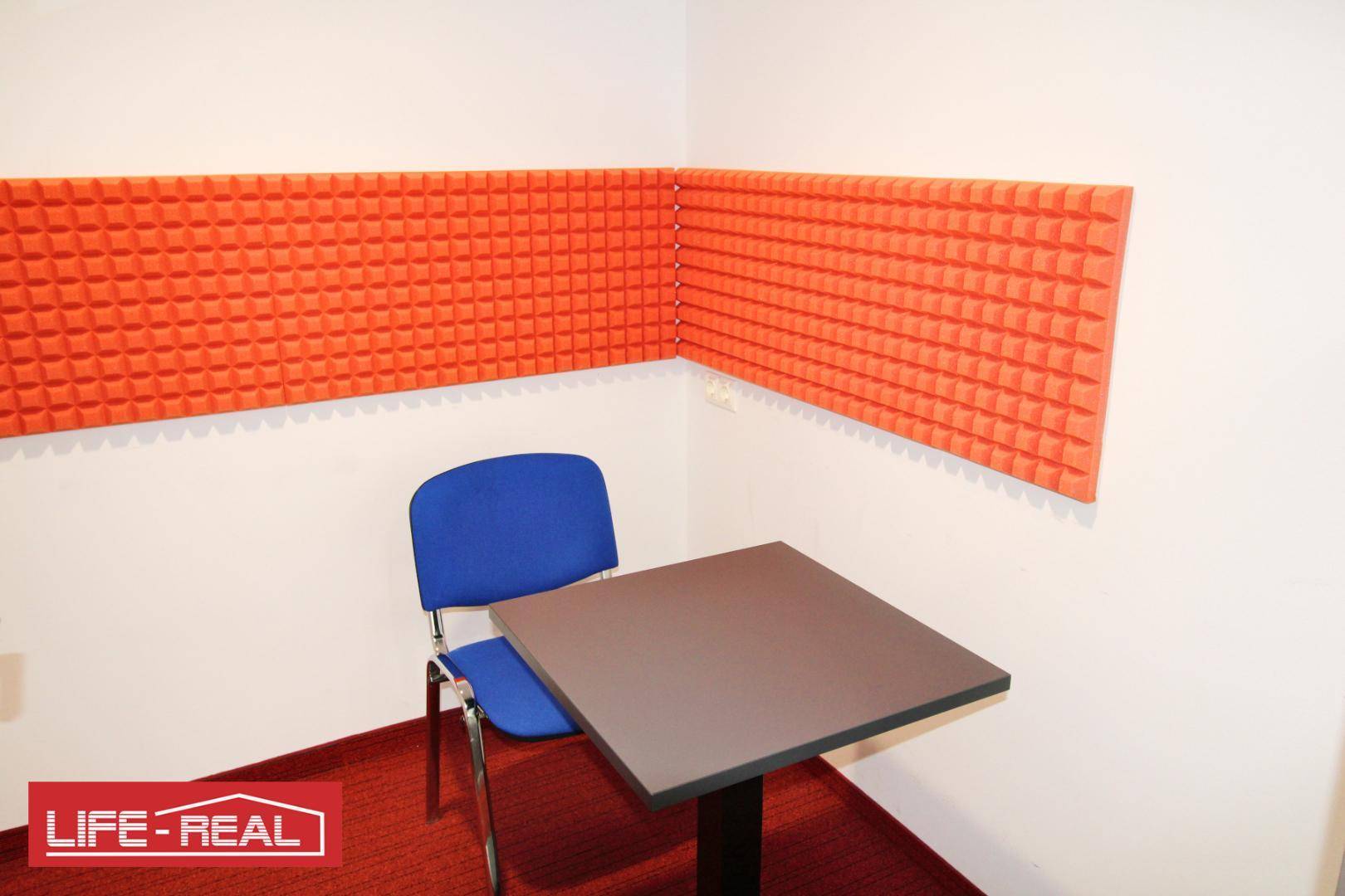 Kompakter Besprechungsraum mit blauer Bestuhlung, kleinem Tisch und schallabsorbierenden orangefarbenen Wandpaneelen.
