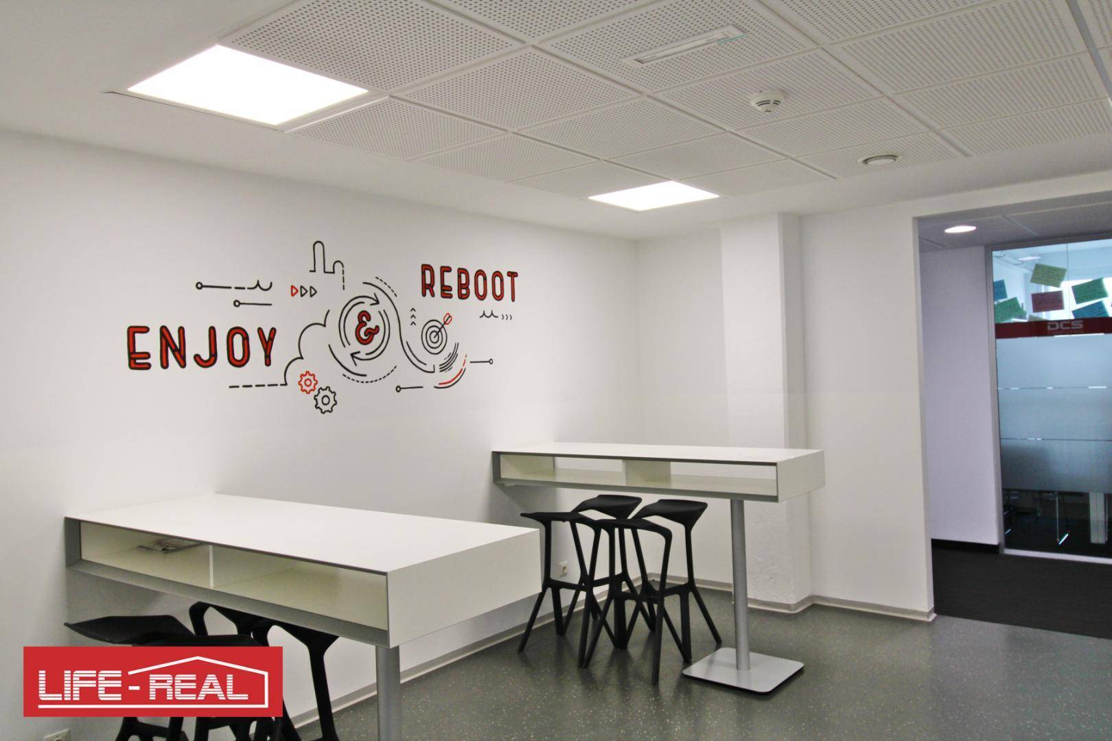 Kreativer Pausenbereich mit hohen Tischen, Barhockern und inspirierender Wandkunst in modernem Design.