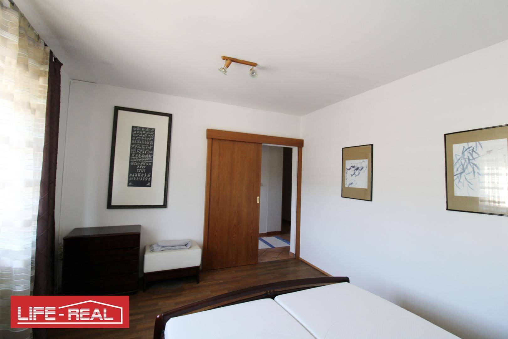 Schlafzimmer mit Holzboden, Doppelbett und Zugang zu einem weiteren Raum durch eine Schiebetür.