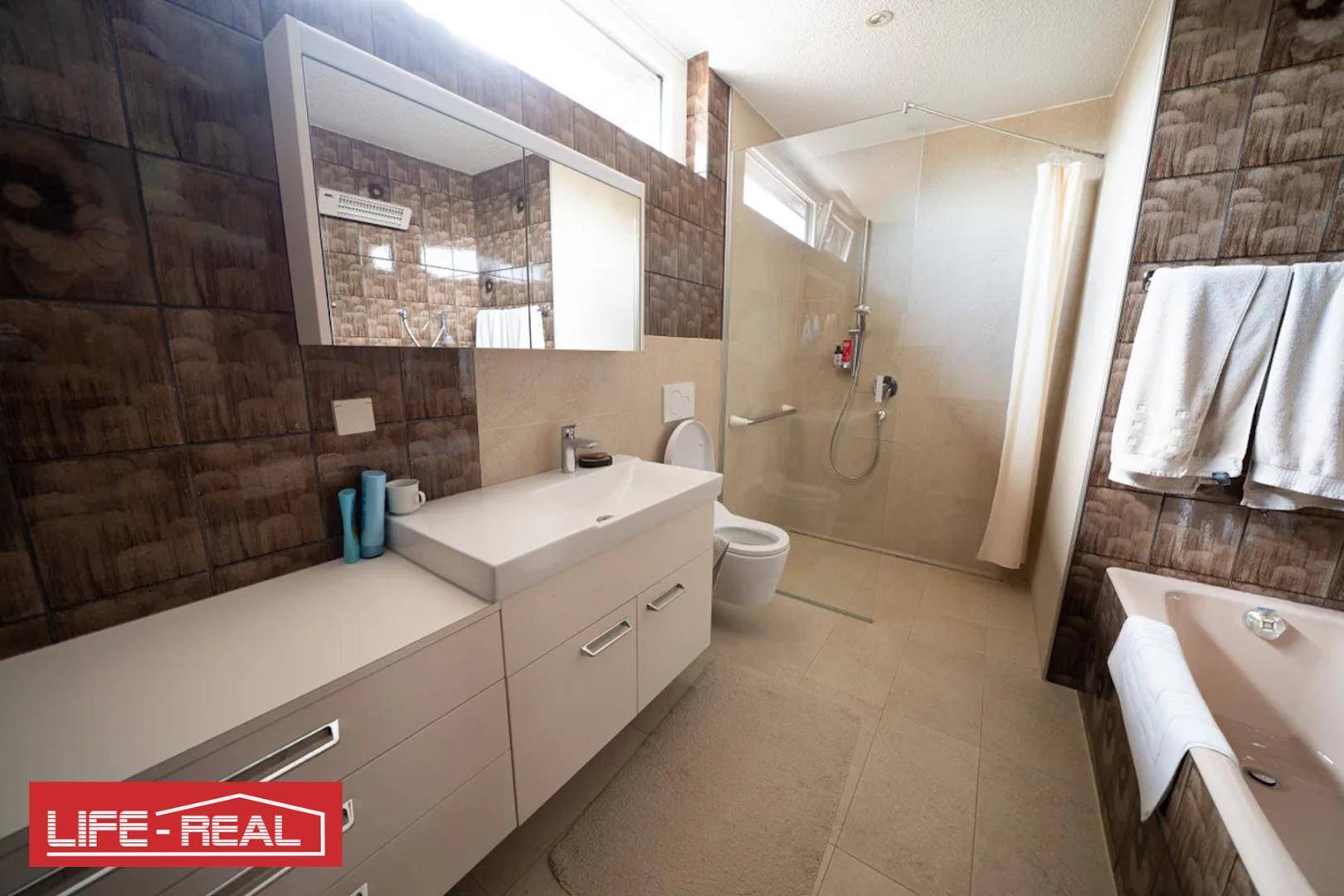 Modernes Badezimmer mit Dusche, Badewanne und stilvollen braunen Fliesen.