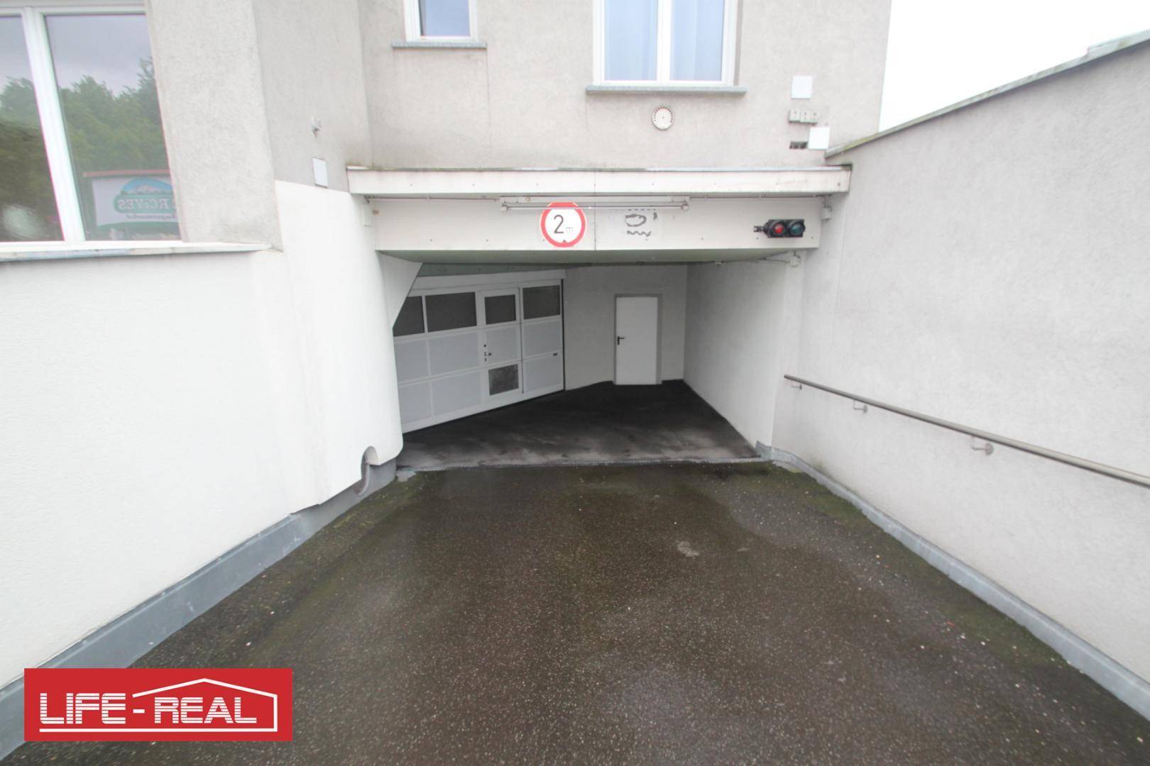 Einfahrt zu einer Tiefgarage mit Rampe und Hinweisschildern an der Decke.