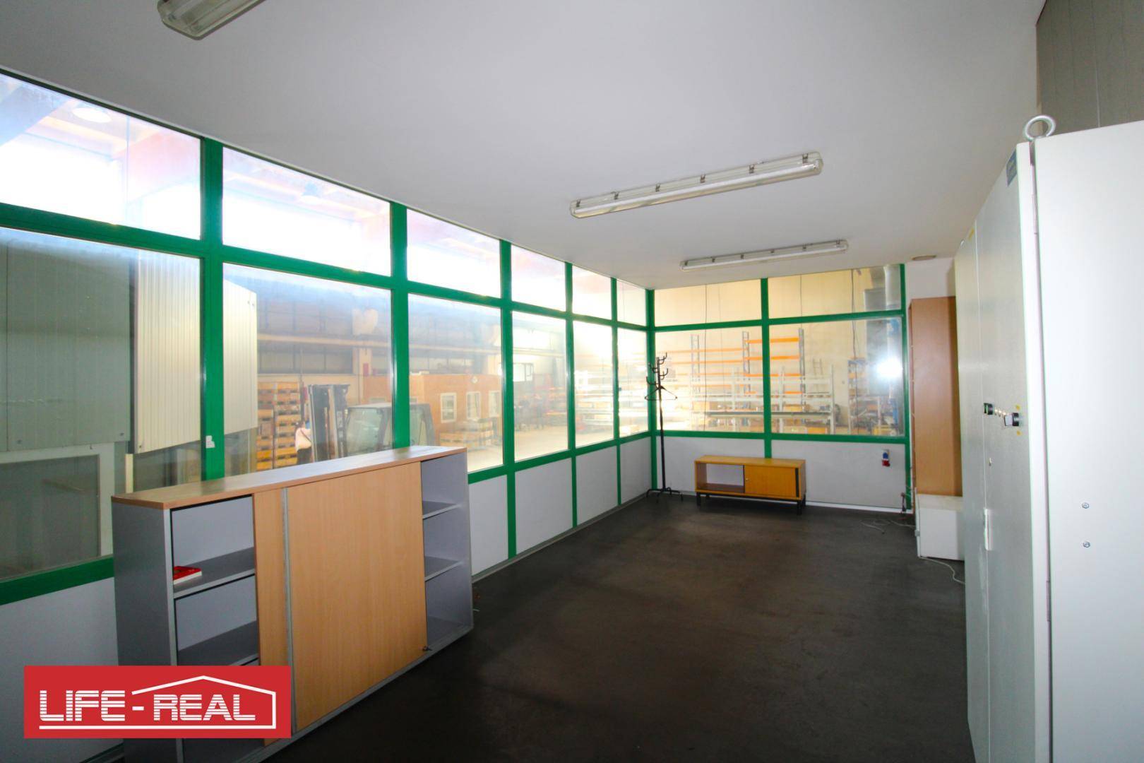 Helles Büro mit großen Fenstern, Schränken und dunklem Bodenbelag innerhalb eines Industriebaus.