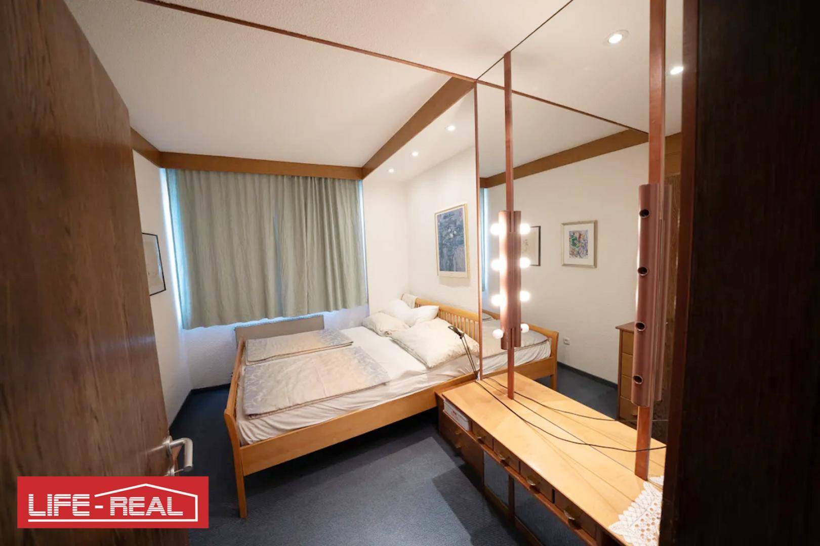 Schlafzimmer mit Doppelbett, Teppichboden und einem großen Spiegel mit Beleuchtung.