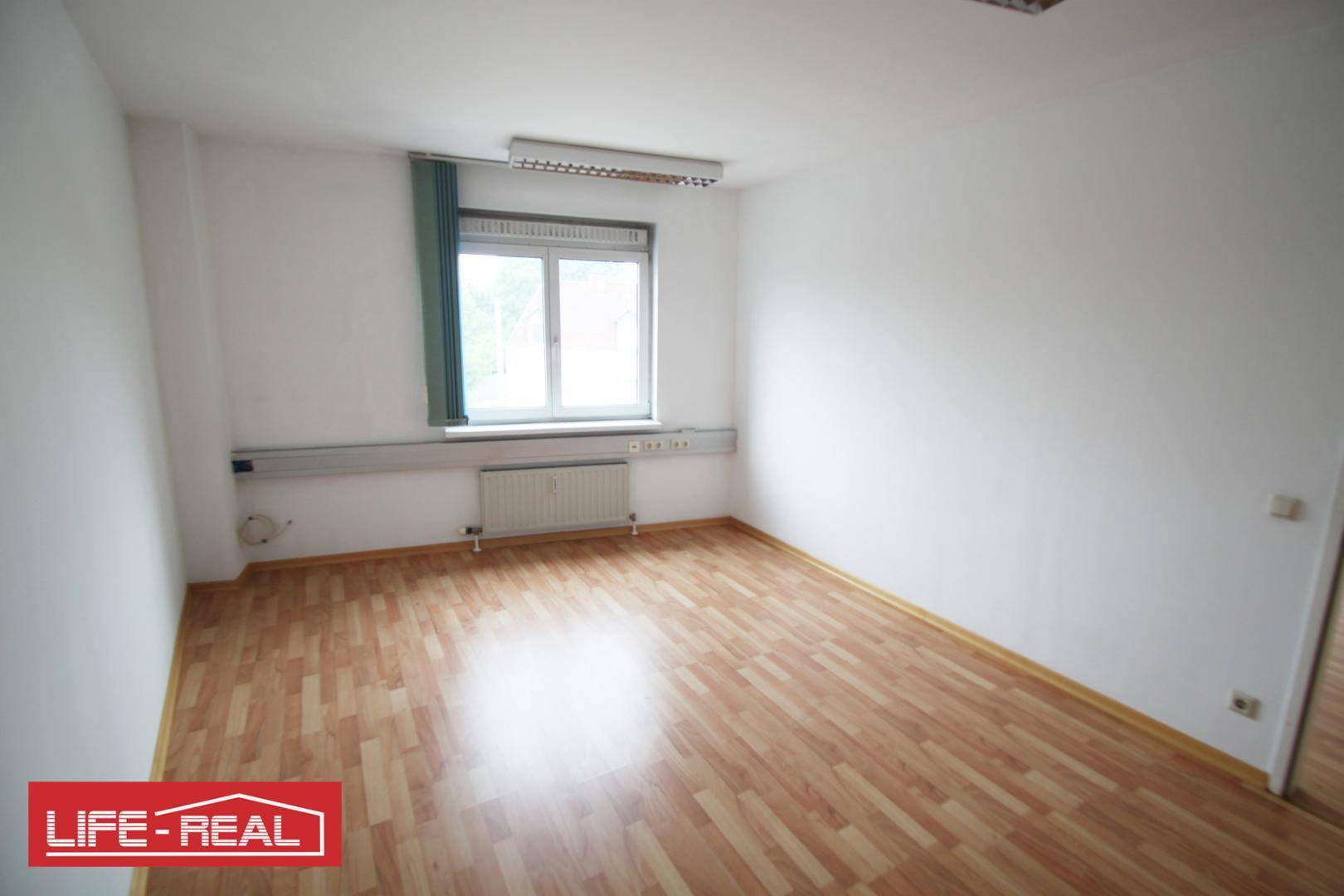 Kleinerer Büroraum mit einem Fenster, Laminatboden und weißen Wänden, ideal für Einzelbüros.