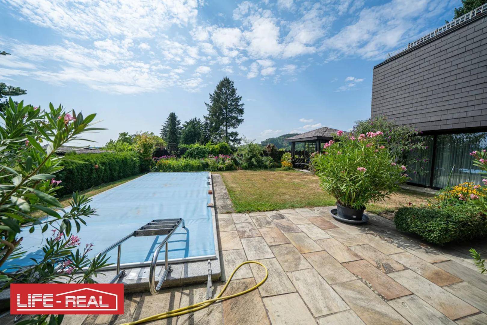 Gepflasterte Terrasse neben dem Pool mit Blick auf die grüne Umgebung und den Gartenpavillon.