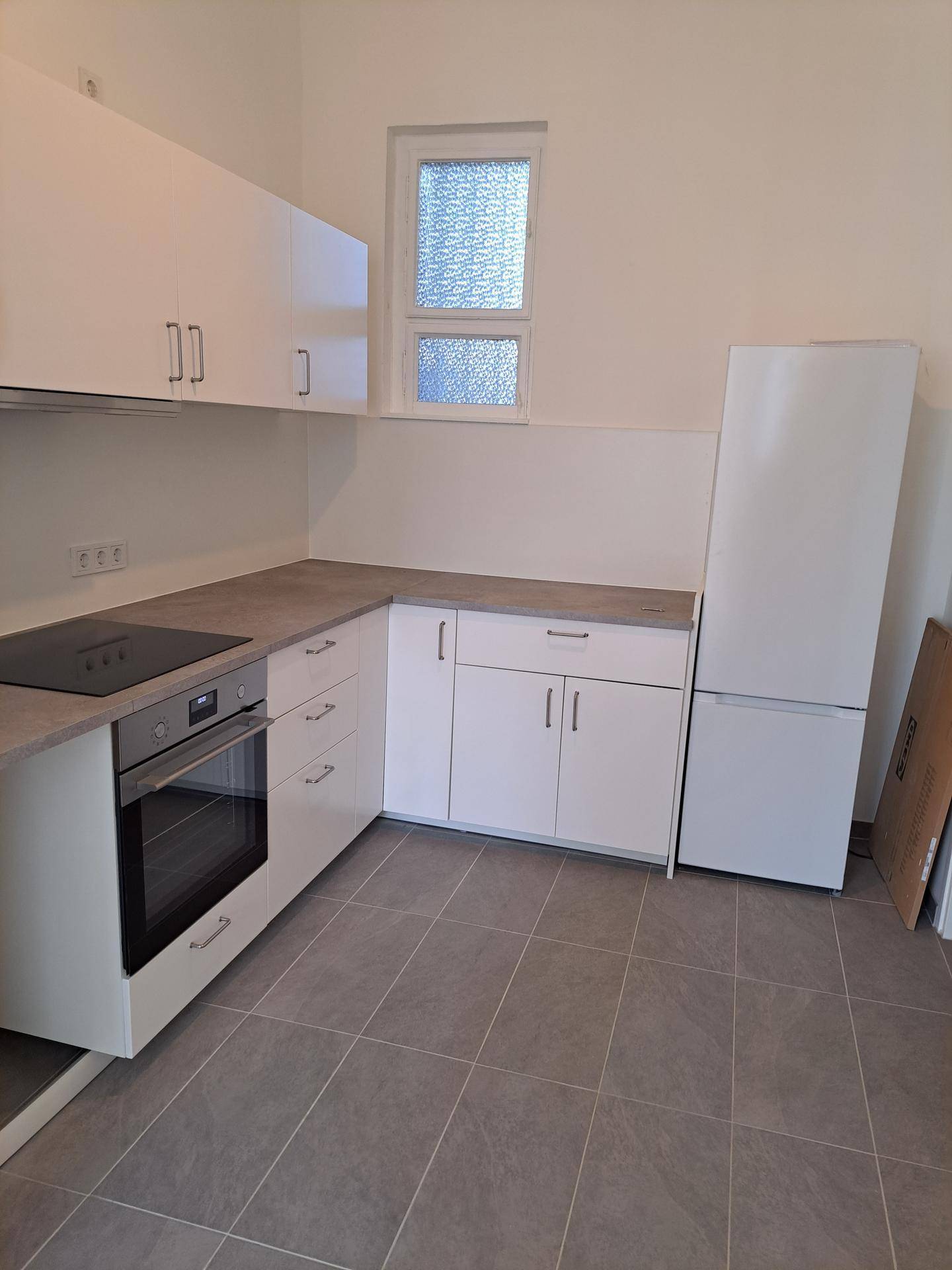 Moderne Küche mit weißen Schränken, Kochfeld, Backofen und Platz für einen Kühlschrank.