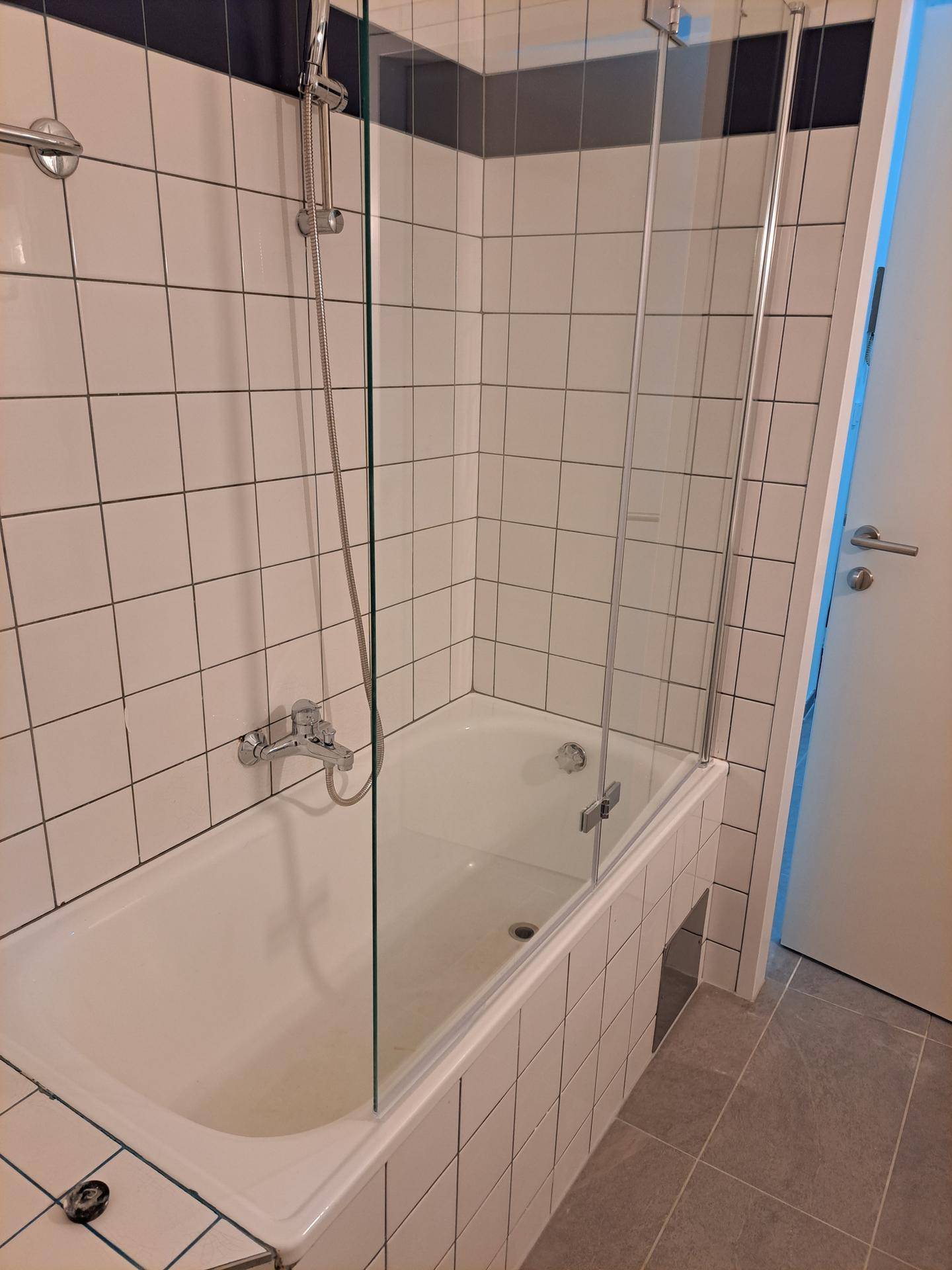 Badewanne mit Duschvorrichtung und Glasabtrennung in einem gefliesten Badezimmer.