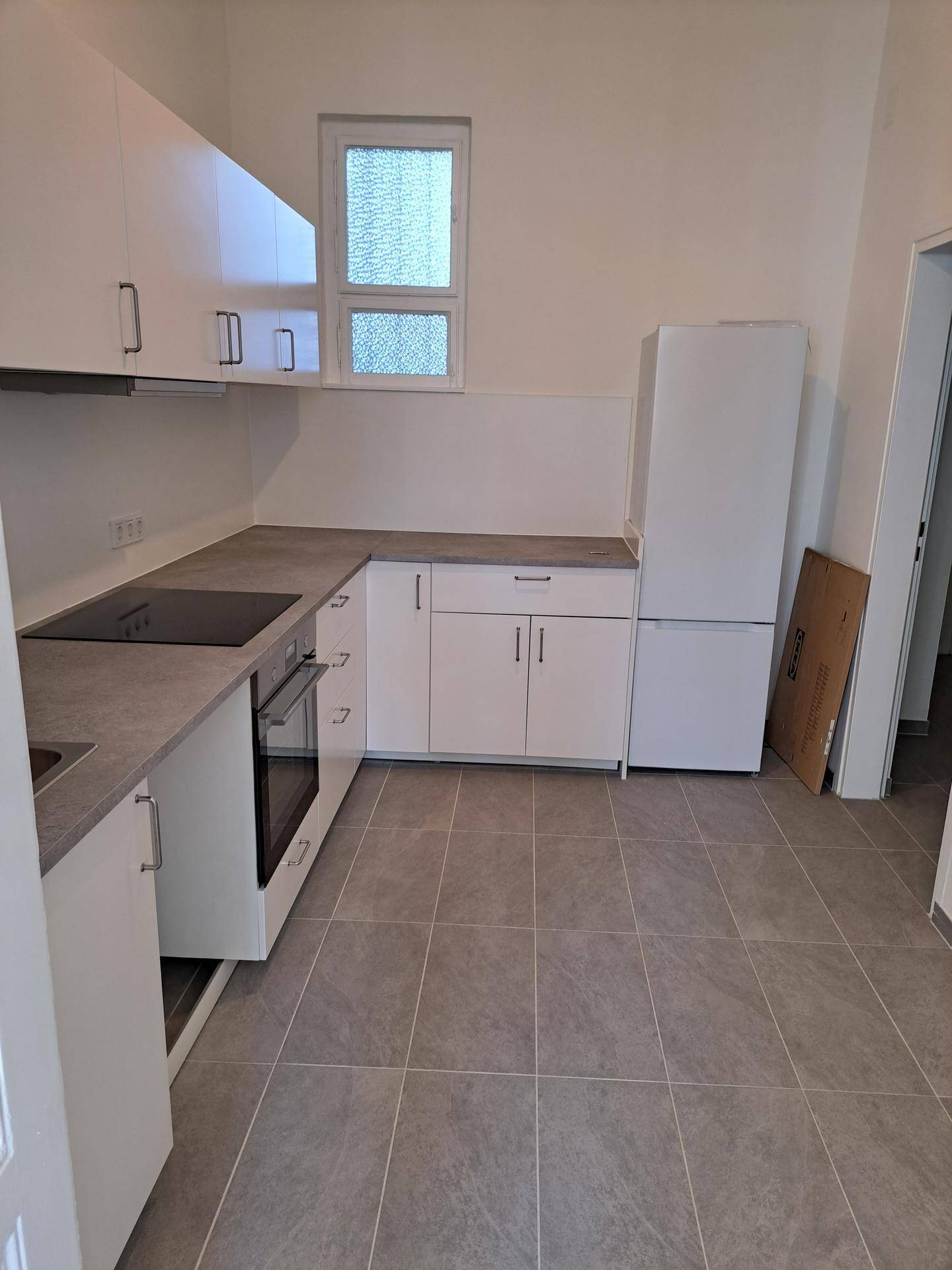 Winkelküche mit weißen Unterschränken, Kochfeld, Backofen und einem freistehenden Kühlschrank.