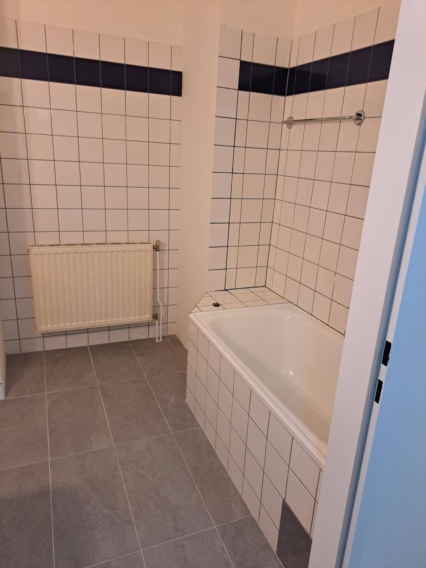 Badezimmer mit integrierter Badewanne und weiß-grauen Fliesen, bereit zur Nutzung.