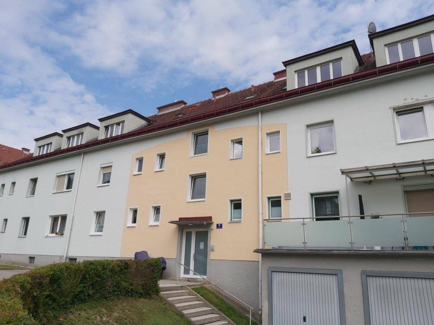 Mehrfamilienhaus mit moderner Fassade, Balkonen und Garagen.