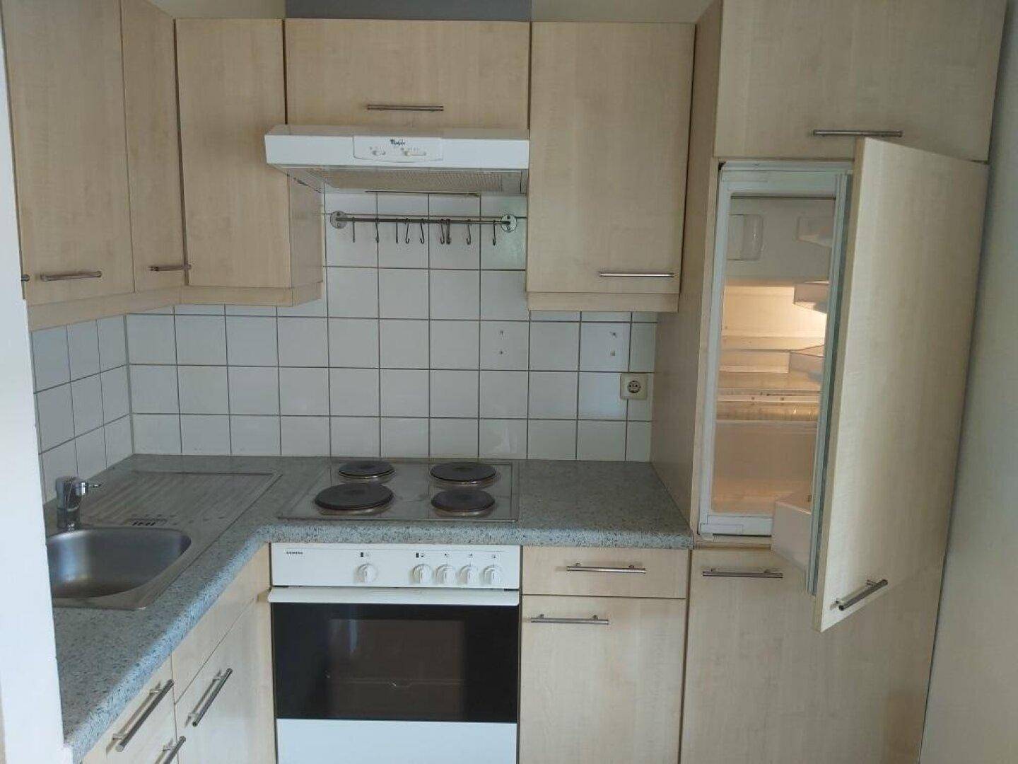 Kleine Einbauküche mit hellen Holzfronten, Herd, Spüle und Kühlschrank.
