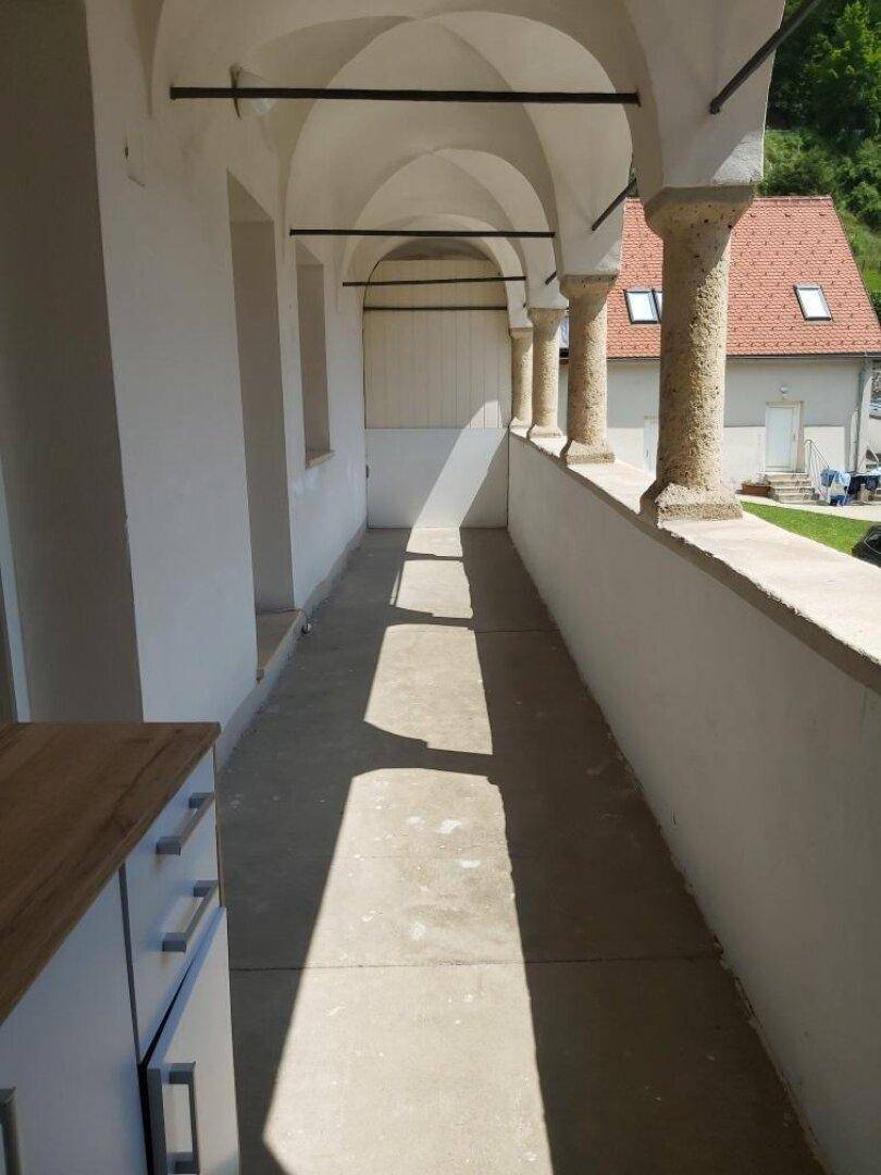 Lange Loggia mit historischen Steinbögen und Säulen, die Schatten spendet.