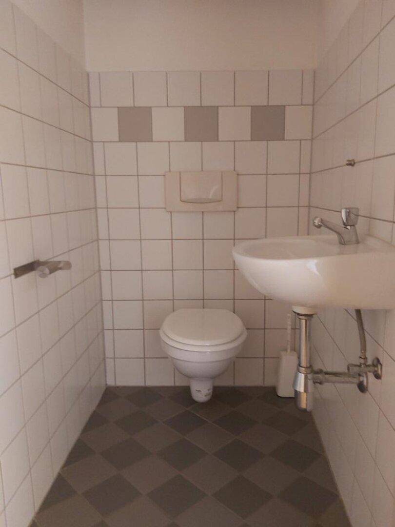 Separates WC mit Toilette, kleinem Waschbecken und weißen Fliesen.