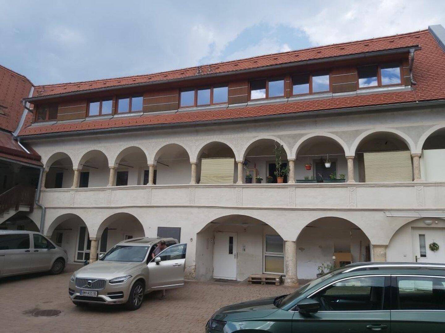 Historisches Gebäude mit Arkaden und einem Innenhof, in dem Autos parken.