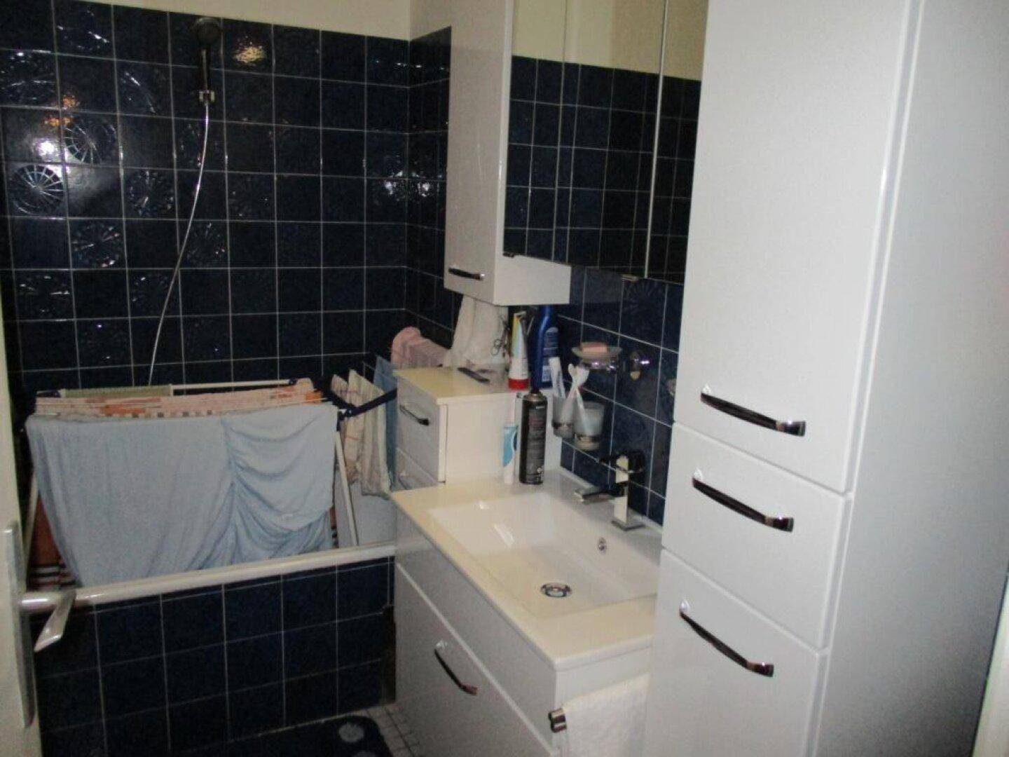 Badezimmer mit dunklen Fliesen, Badewanne und Waschbecken mit Spiegelschrank.