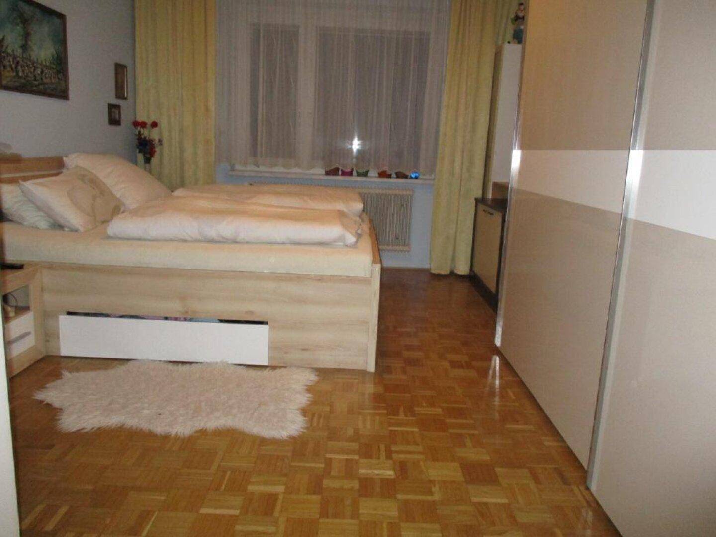 Schlafzimmer mit hellem Parkettboden, Doppelbett und großem Kleiderschrank.