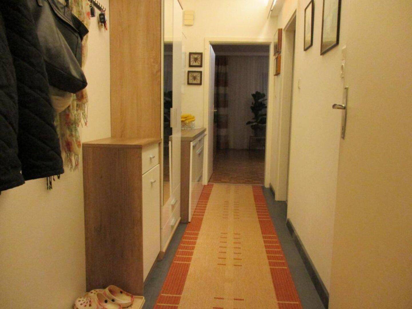 Heller Flur mit Garderobe, Spiegel und Teppichläufer, der zu weiteren Räumen führt.