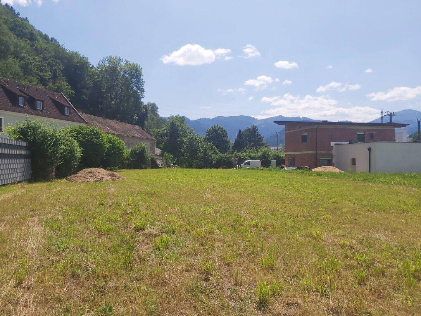 Offenes Wiesengrundstück mit Blick auf die umliegende Berglandschaft und Nachbarhäuser bei Tag.