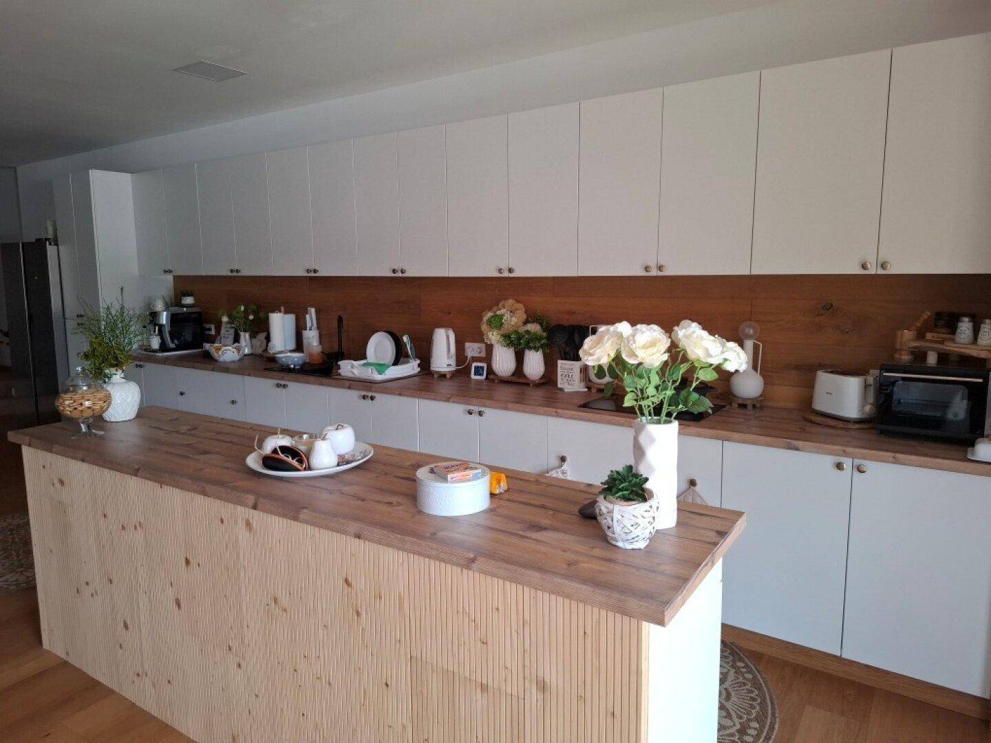 Moderne Küche mit weißen Schränken, Holztheke und viel Arbeitsfläche.