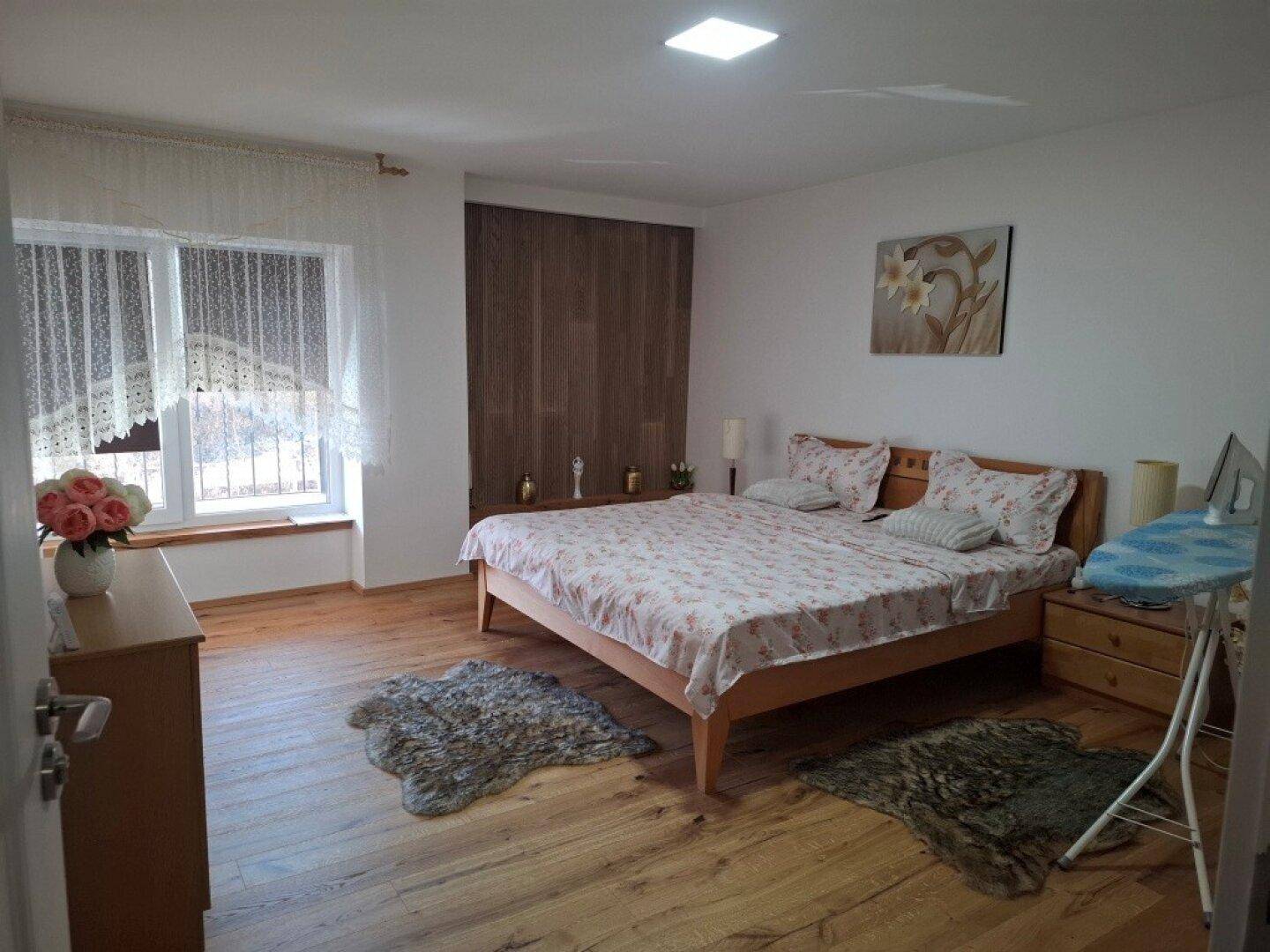 Helles Schlafzimmer mit Holzbett, Parkettboden und großem Fenster.