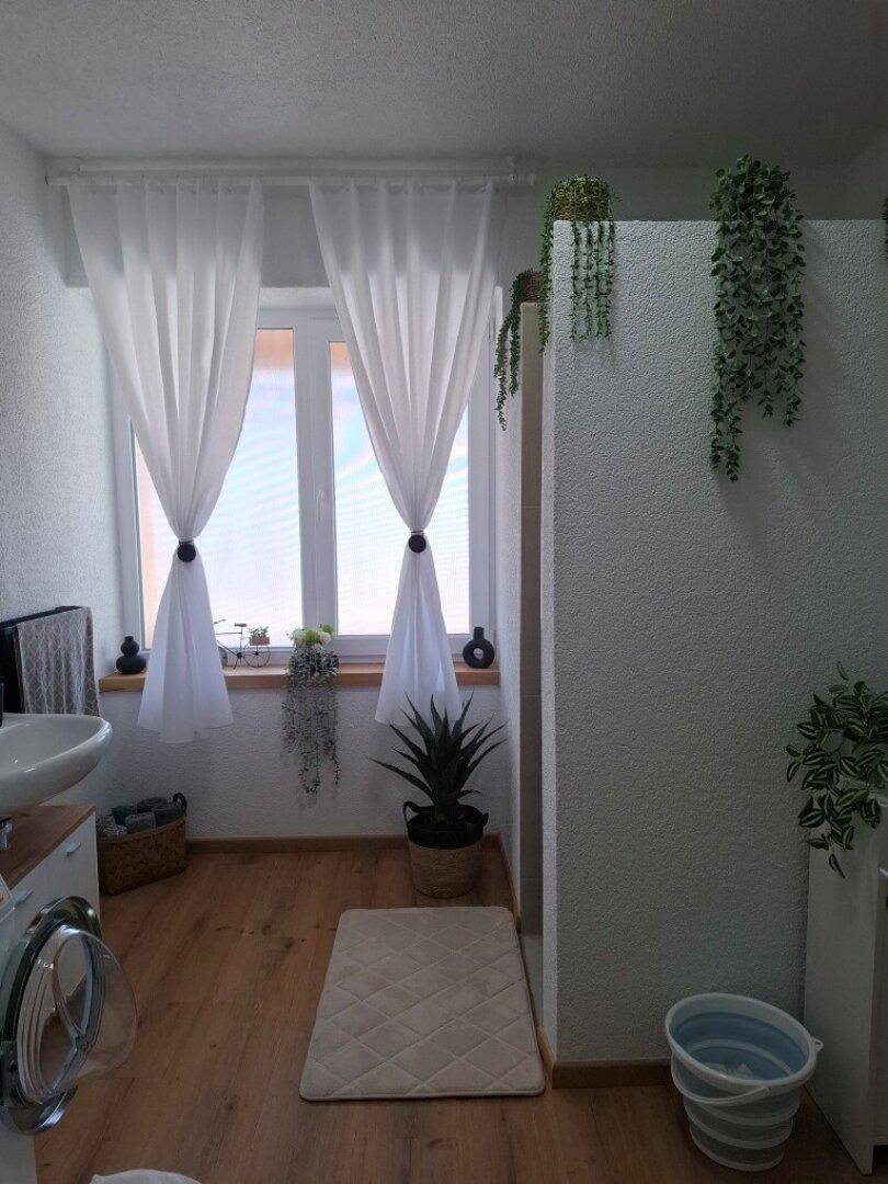 Helles Badezimmer mit Fenster, Waschmaschine und dekorativen Pflanzen.