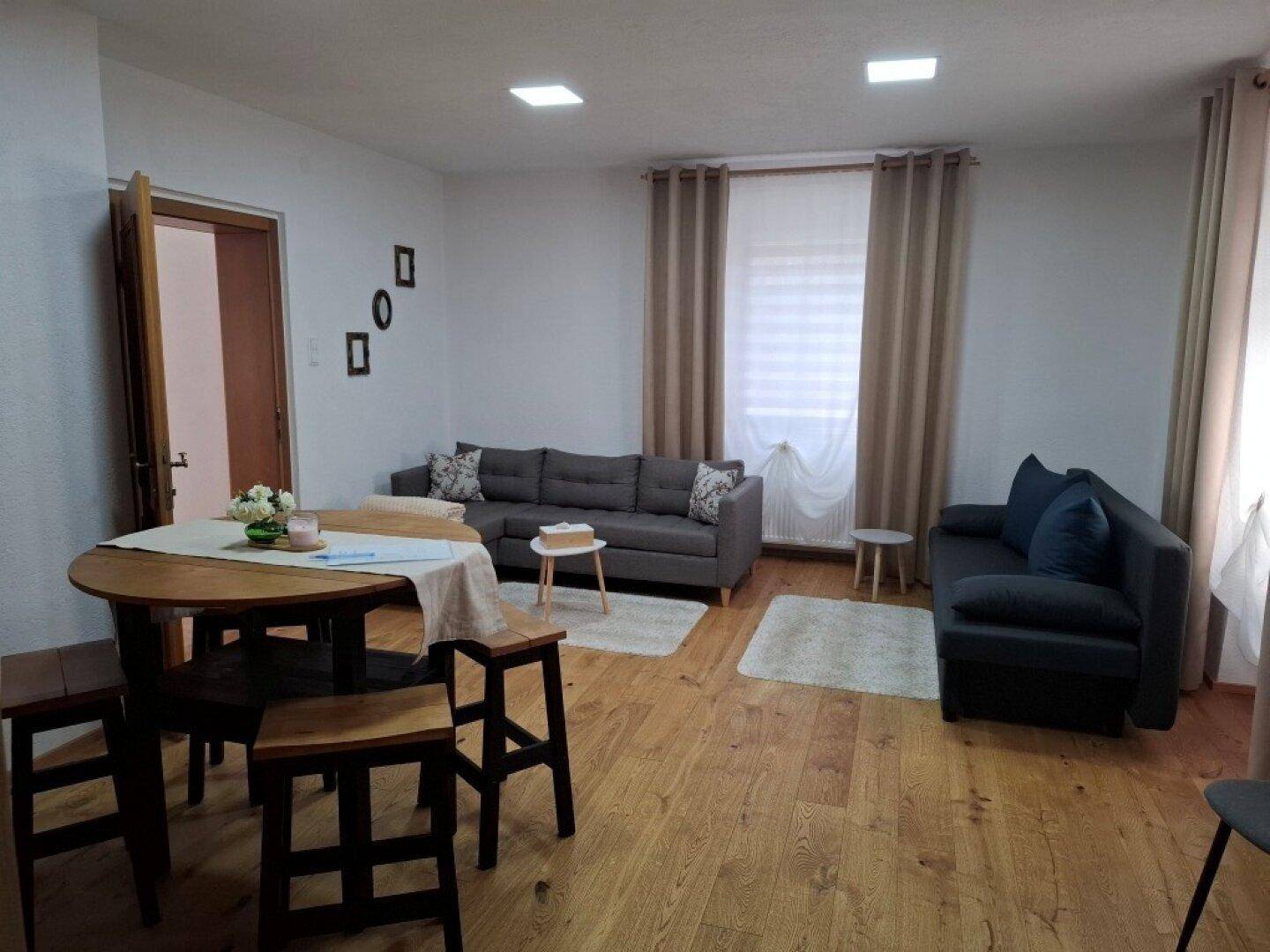 Gemütliches Wohnzimmer mit Sofa, Esstisch und Parkettboden.