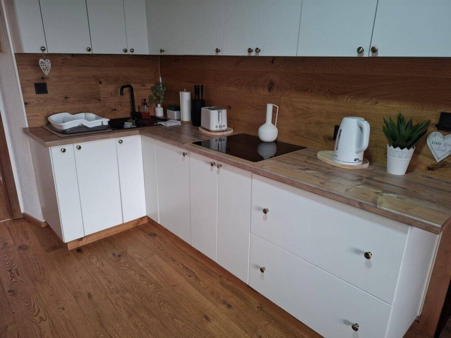 Moderne weiße Küche mit Holz-Arbeitsplatten und Induktionskochfeld.