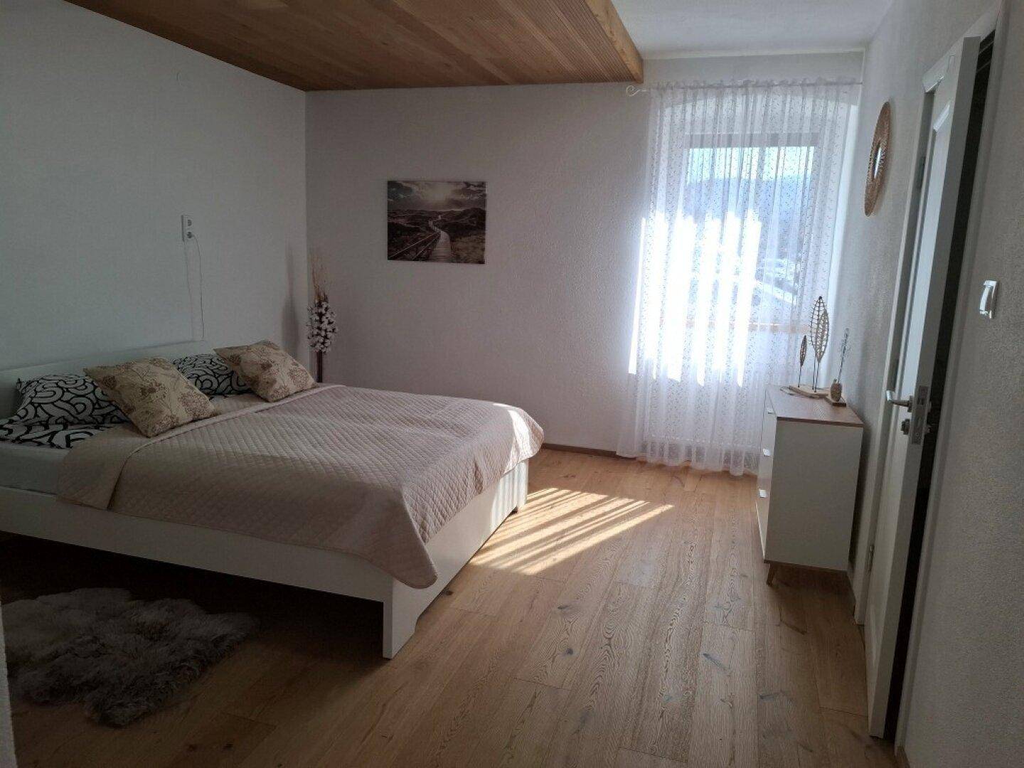 Schlafzimmer mit Doppelbett, Holzbalkendecke und viel Tageslicht.