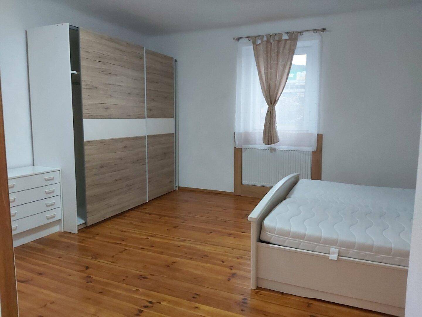 Schlafzimmer mit großem Kleiderschrank, Bett und Parkettboden.