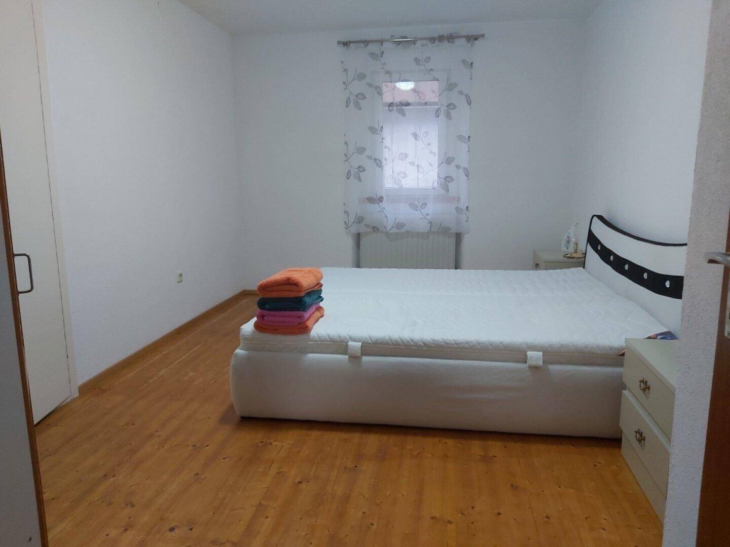 Helles Schlafzimmer mit Doppelbett, Parkettboden und schlichtem Design.