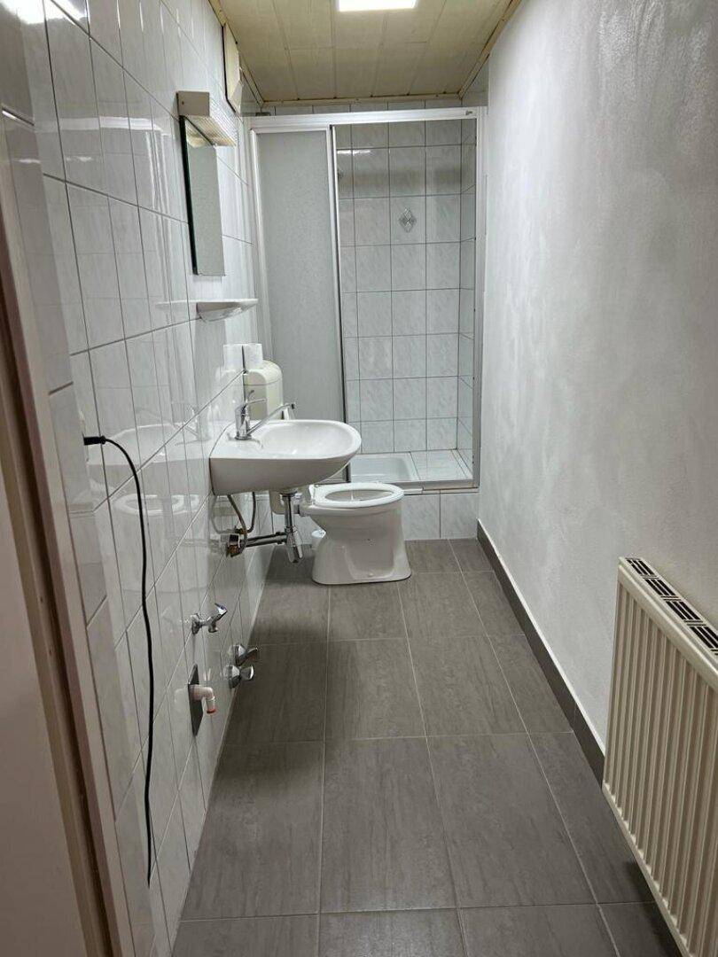 Badezimmer mit Dusche, Waschbecken und grauen Fliesen.