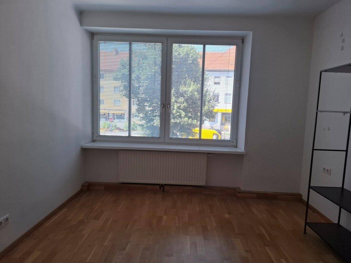 Heller Raum mit Holzfußboden und großem Fenster, das viel Tageslicht hereinlässt.