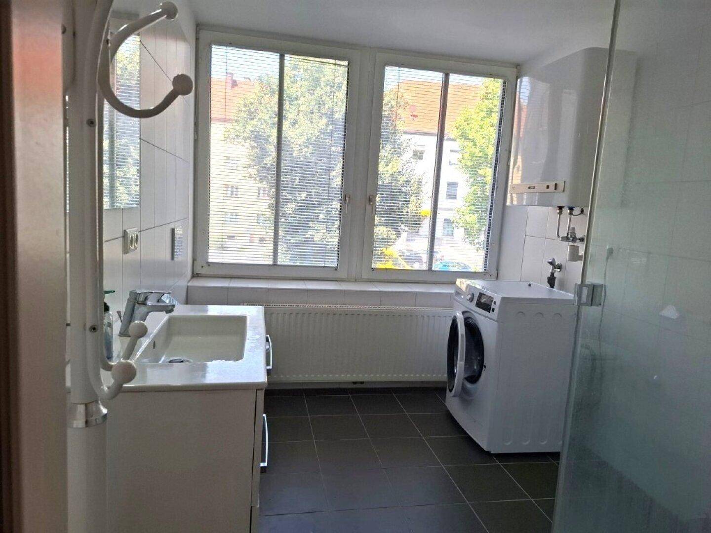 Badezimmer mit Waschbecken, Waschmaschine und großem Fenster für natürliche Belüftung und Helligkeit.