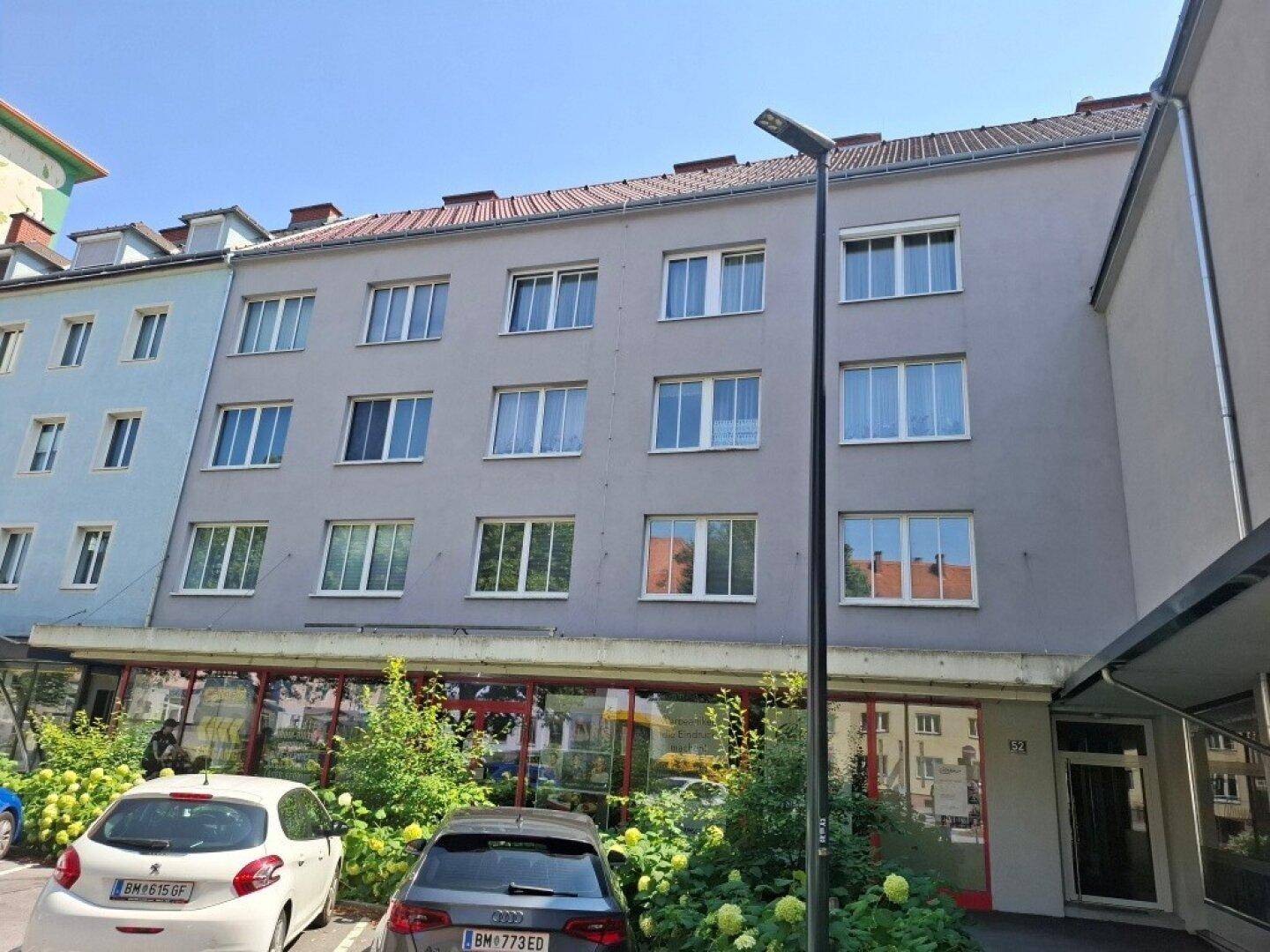 Mehrstöckiges Wohngebäude mit grauer Fassade und Geschäften im Erdgeschoss.