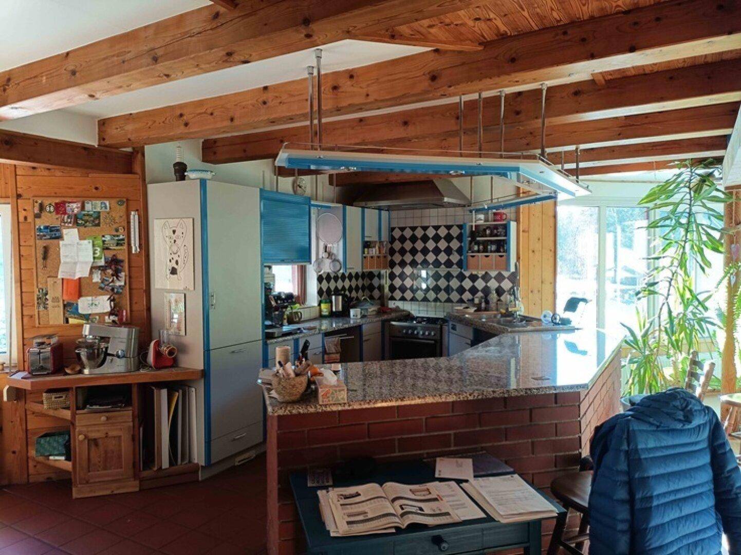 Rustikale Küche mit Ziegeltheke, blauen Schränken und Holzbalkendecke.