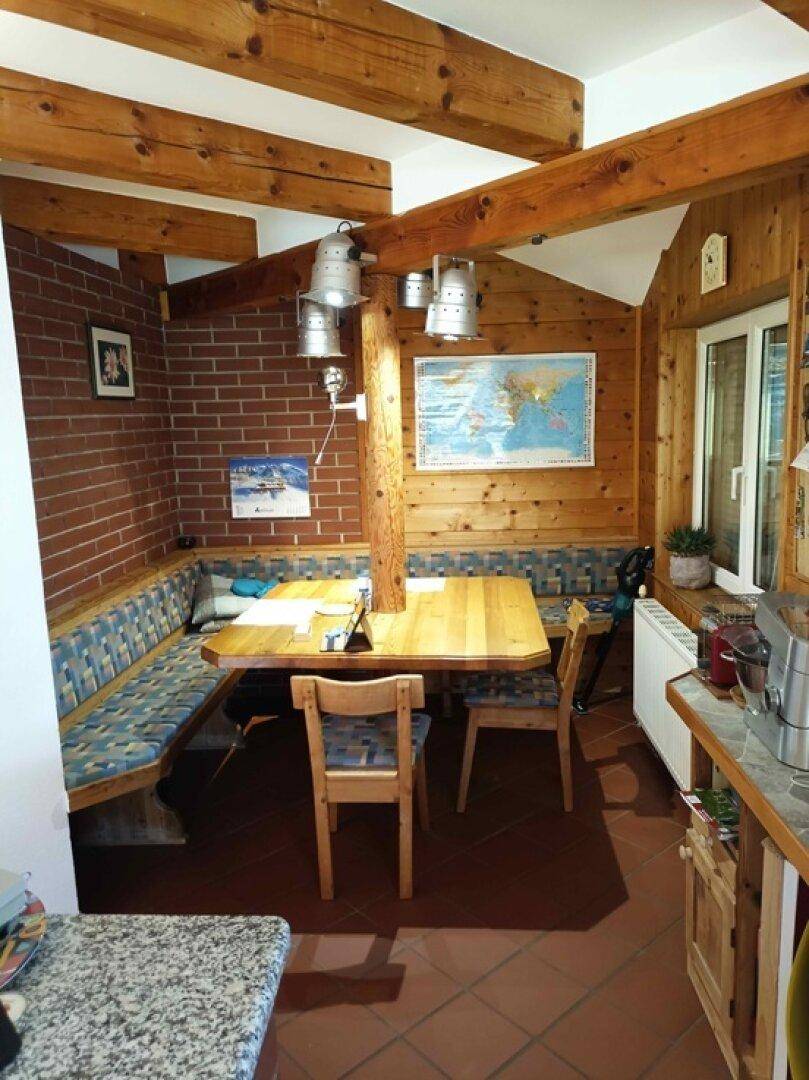 Gemütlicher Essbereich mit Holztisch, Eckbank und Ziegelwand unter Holzbalkendecke.