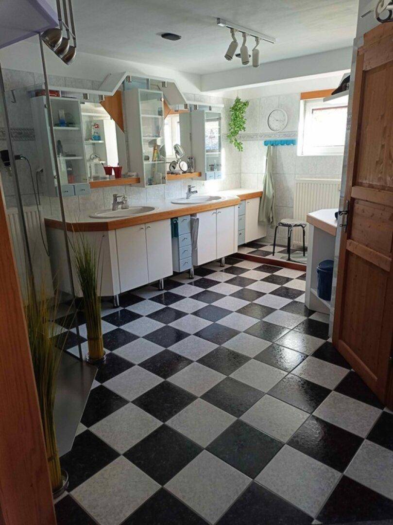 Helles Badezimmer mit Doppelwaschbecken, Fenster und markantem Schachbrettmuster-Fliesenboden.