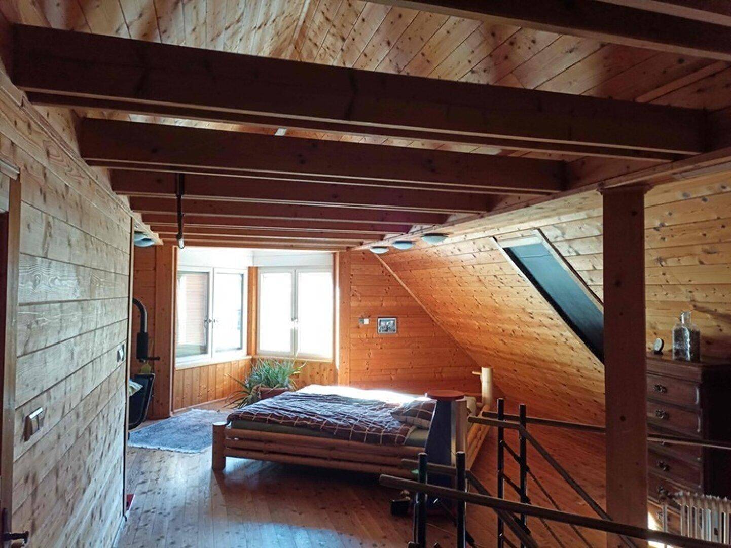 Gemütliches Schlafzimmer im Dachgeschoss mit Holzbalken, Holzwänden und Fenster.