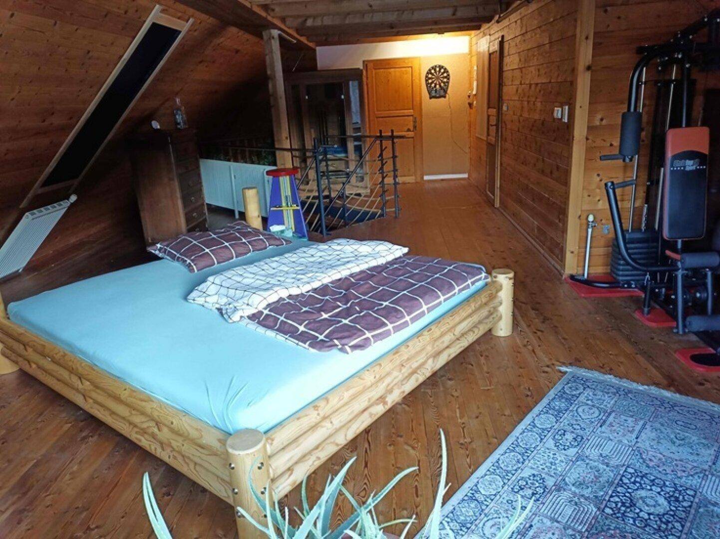 Geräumiges Schlafzimmer im Dachgeschoss mit Holzboden, Holzwänden und Fitnessbereich.