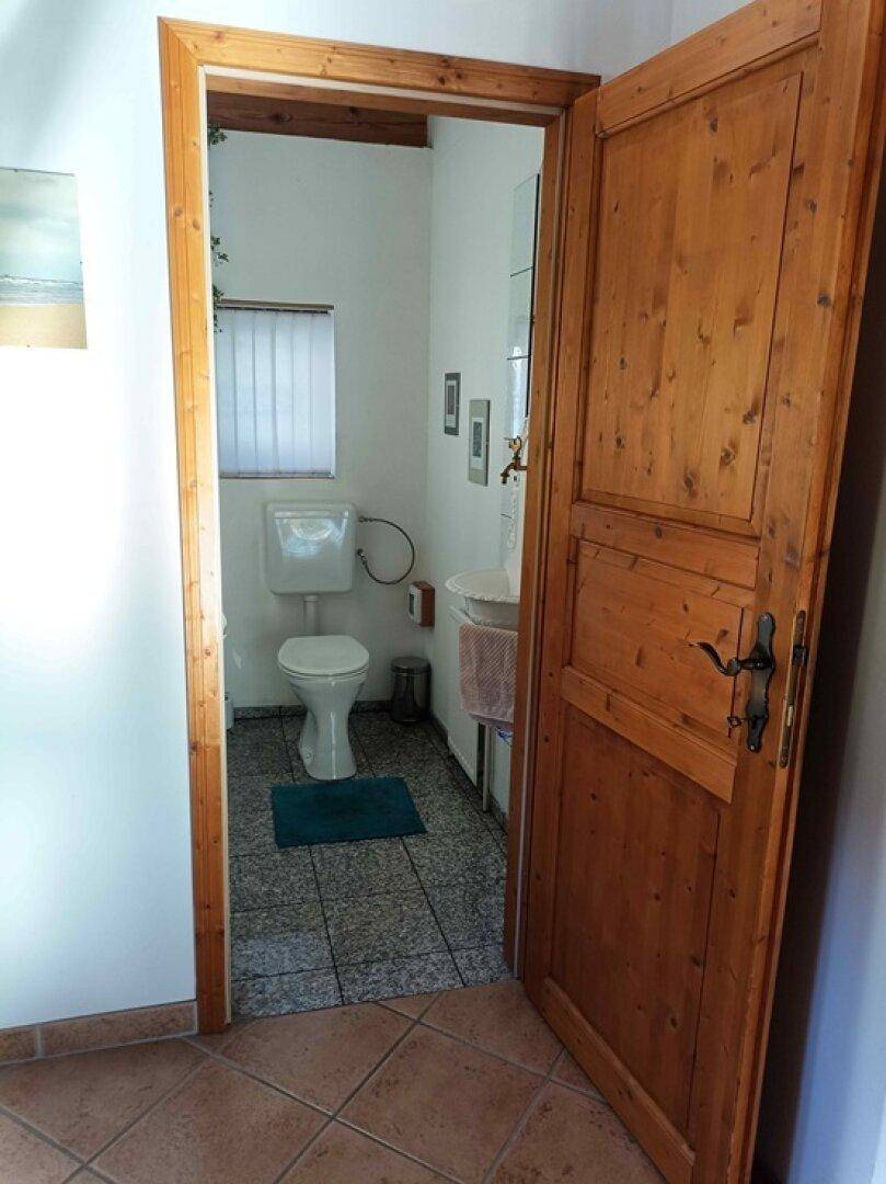 Kleines Gäste-WC mit Fenster, Fliesenboden und Holztür.
