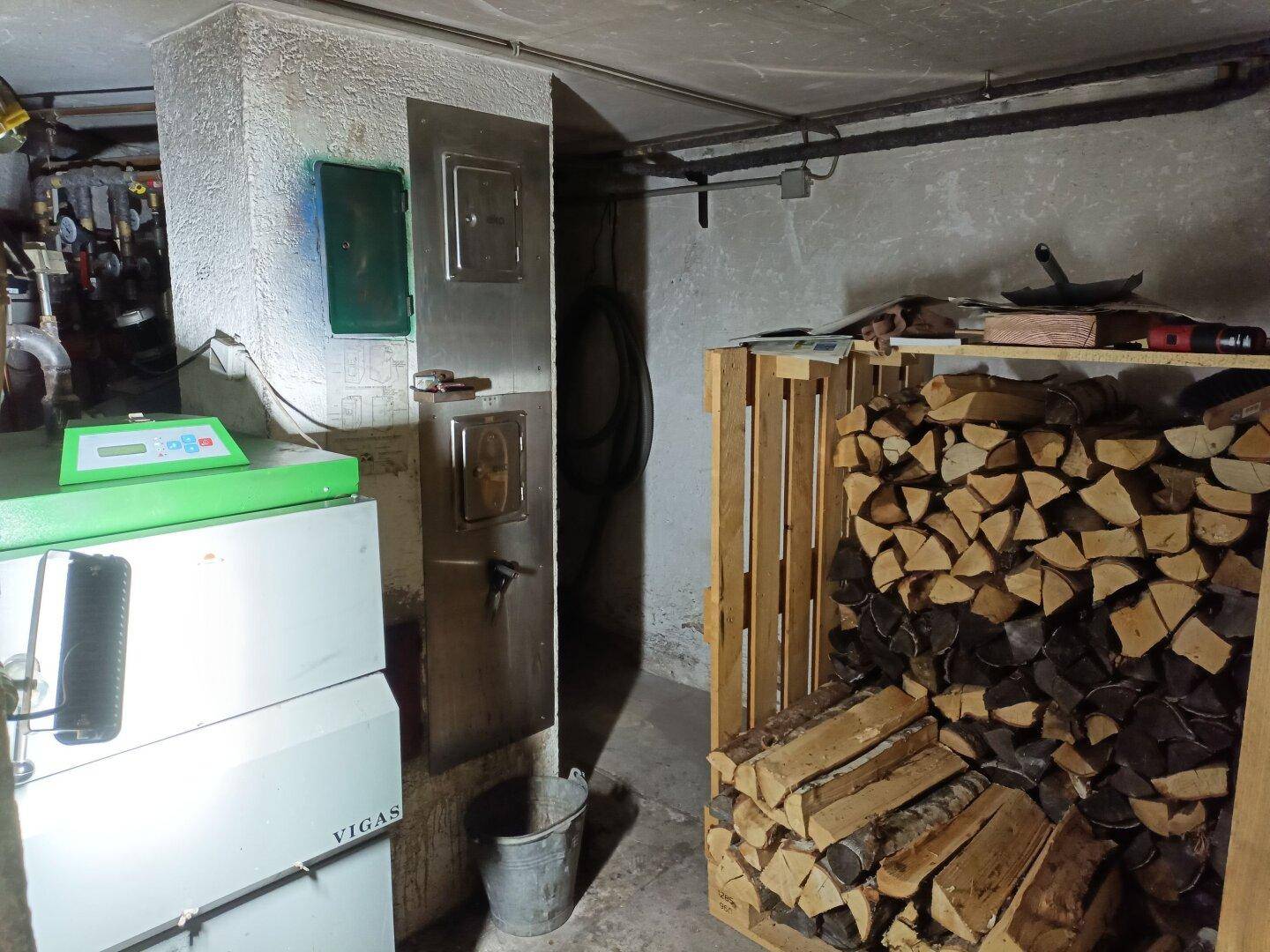 Heizungsraum im Keller mit Holzscheiten für den Ofen und einem modernen Heizkessel.
