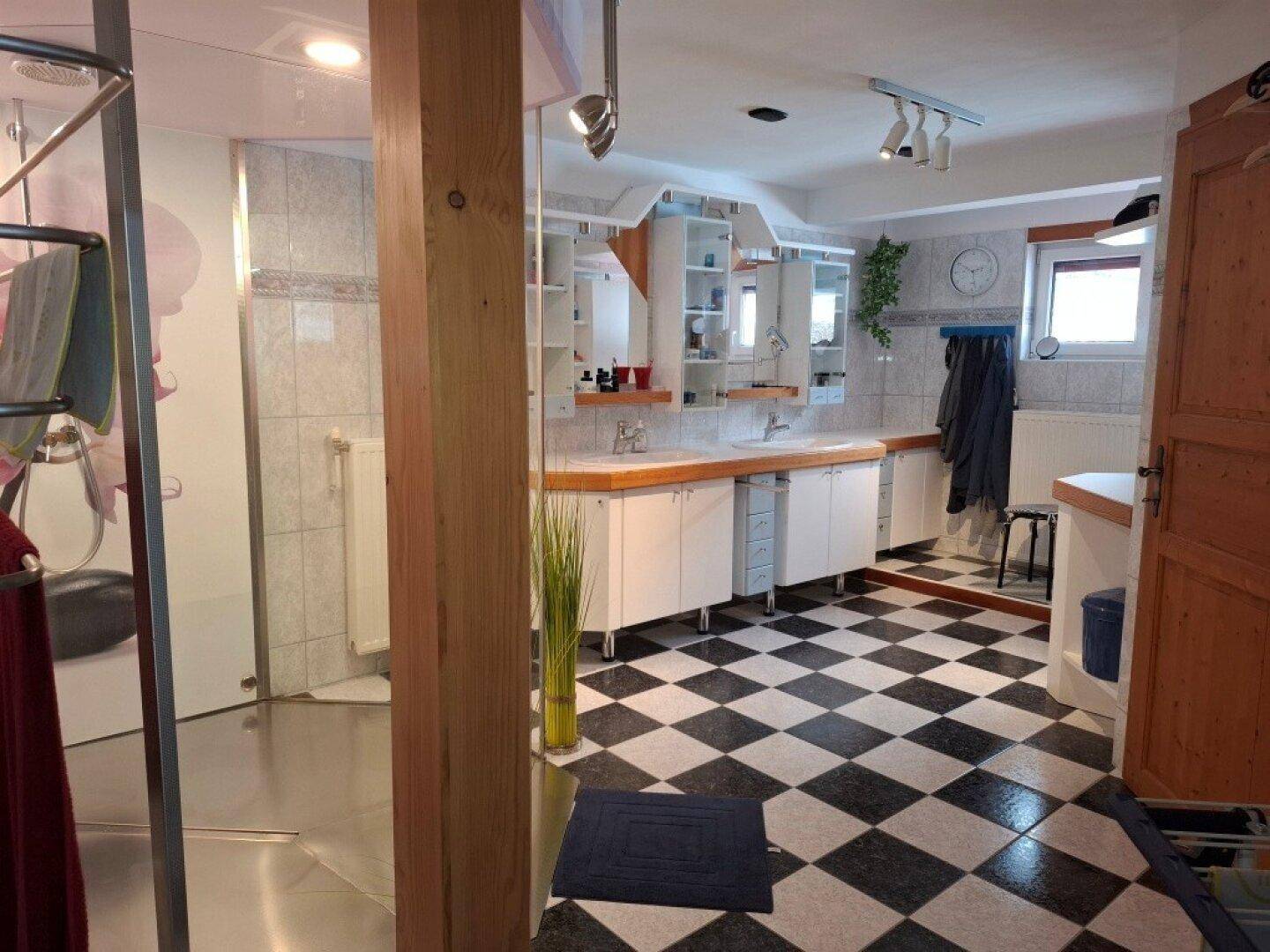 Geräumiges Badezimmer mit schwarz-weißem Schachbrettmuster-Fliesenboden und Doppelwaschbecken.