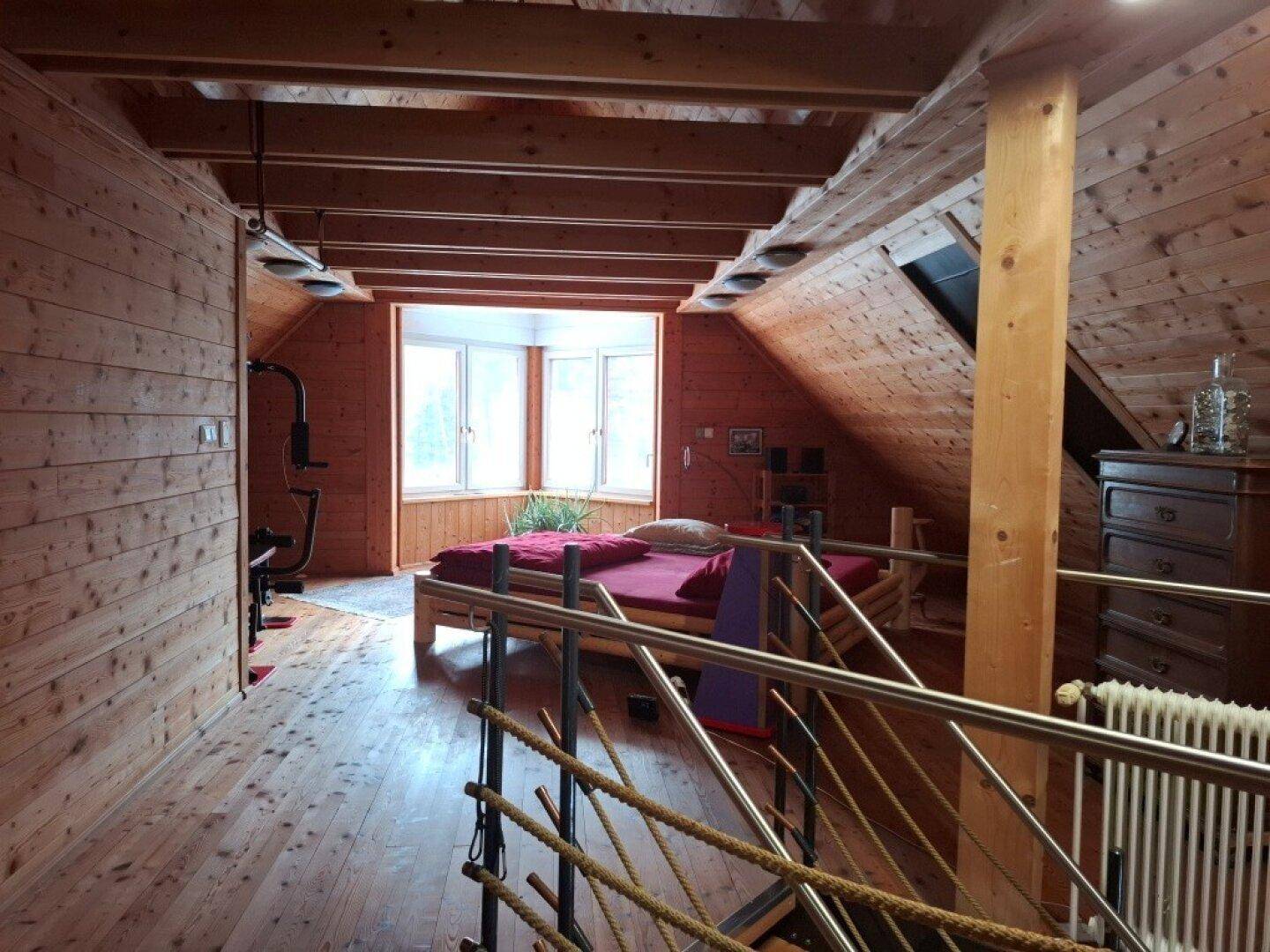 Gemütliches Schlafzimmer im Dachgeschoss mit Holzverkleidung, Holzboden und großen Fenstern.