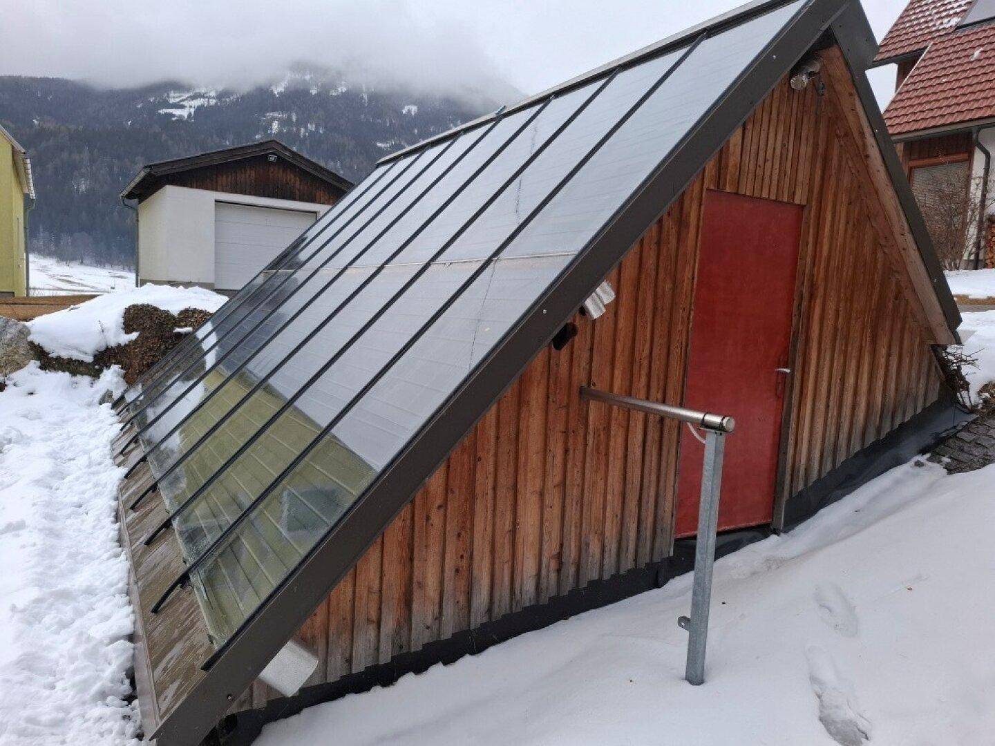 Kleines Nebengebäude mit Solarpaneelen auf dem schrägen Dach, umgeben von Schnee.