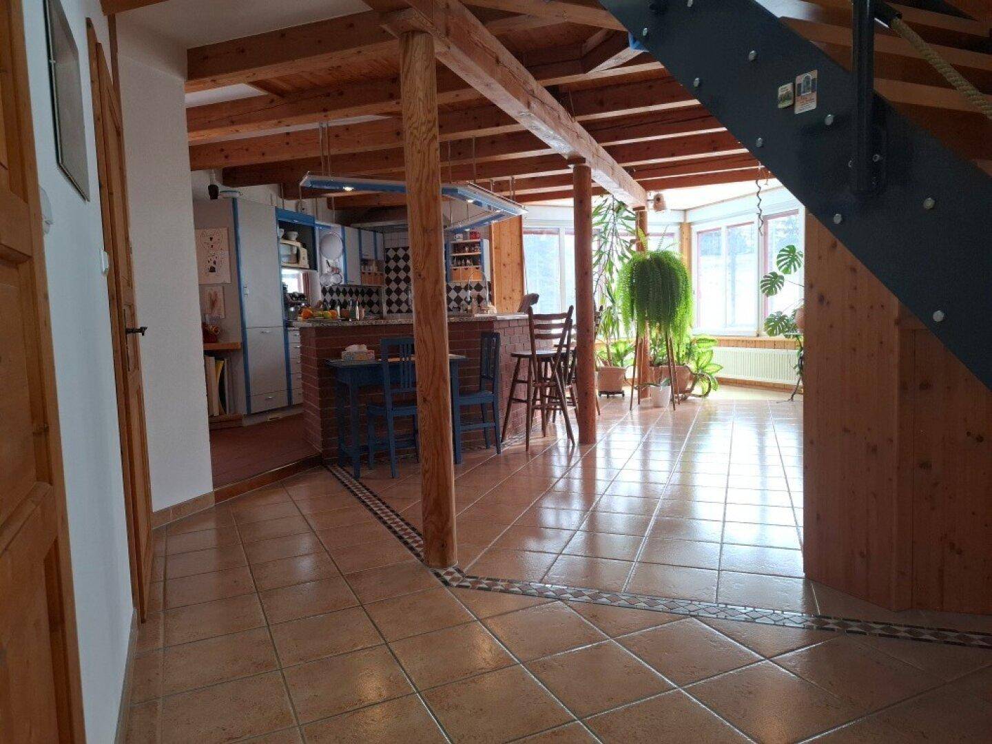 Offener Wohnbereich mit Holzbalken, Fliesenboden und integrierter Bar im Landhausstil.