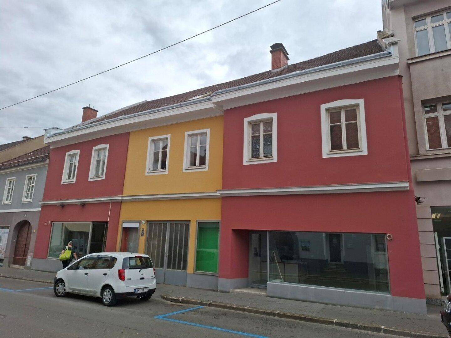 Mehrfarbiges Gebäude mit roter und gelber Fassade, weißen Fenstern und Satteldach an einer Straße.