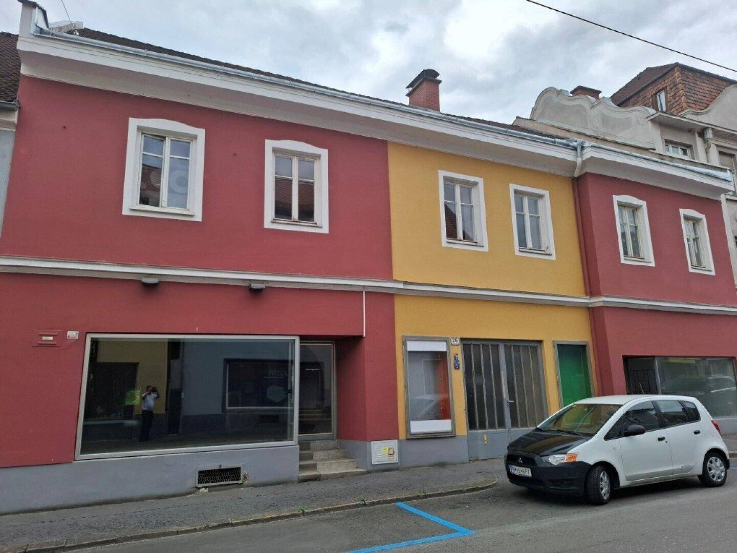 Farbige Fassade eines gut erhaltenen Altbaus mit roten und gelben Abschnitten und traditionellen weißen Fenstern.