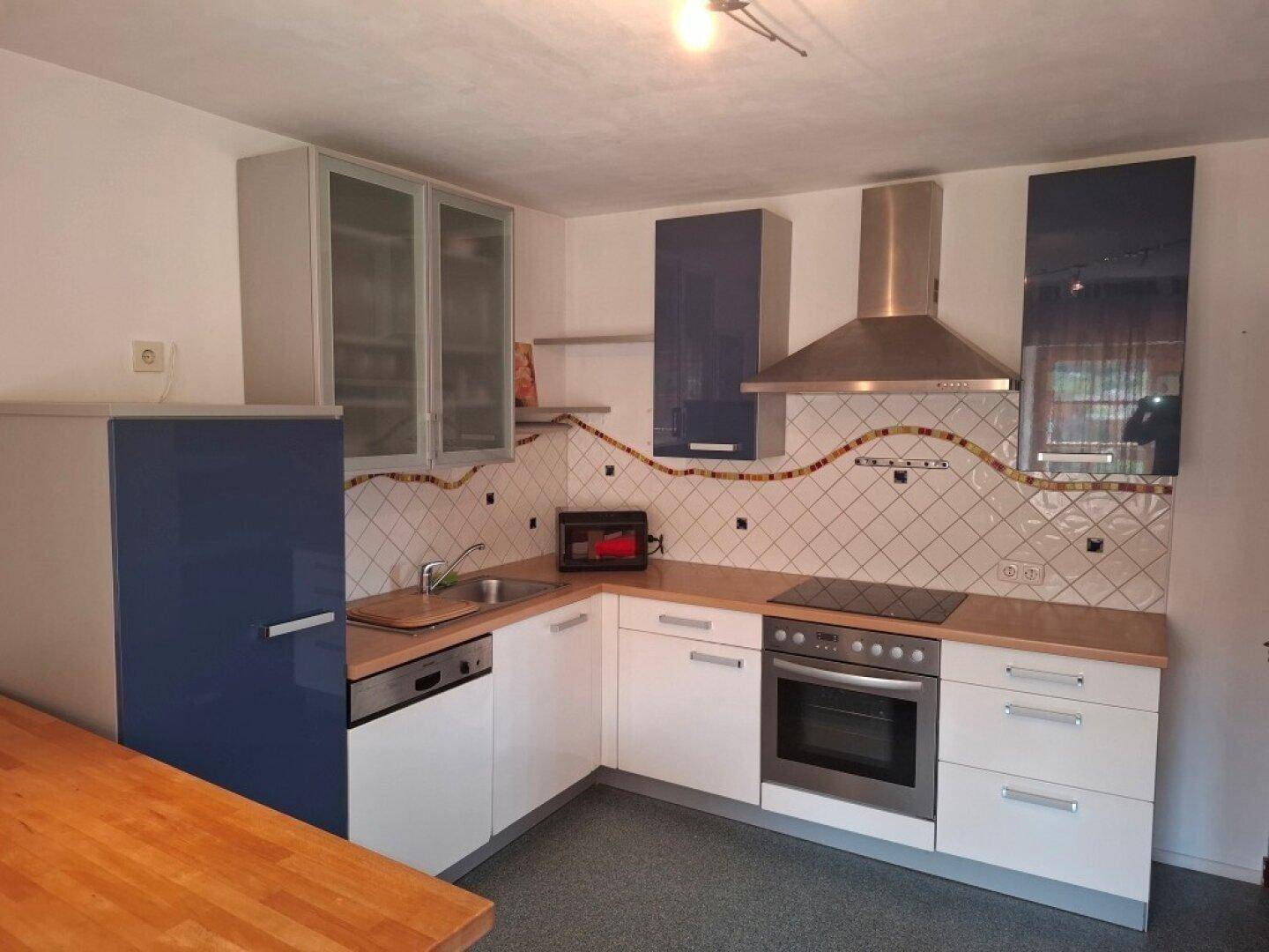 Funktionale Küche mit blauen und weißen Schränken, integrierten Geräten und Fliesenrückwand.