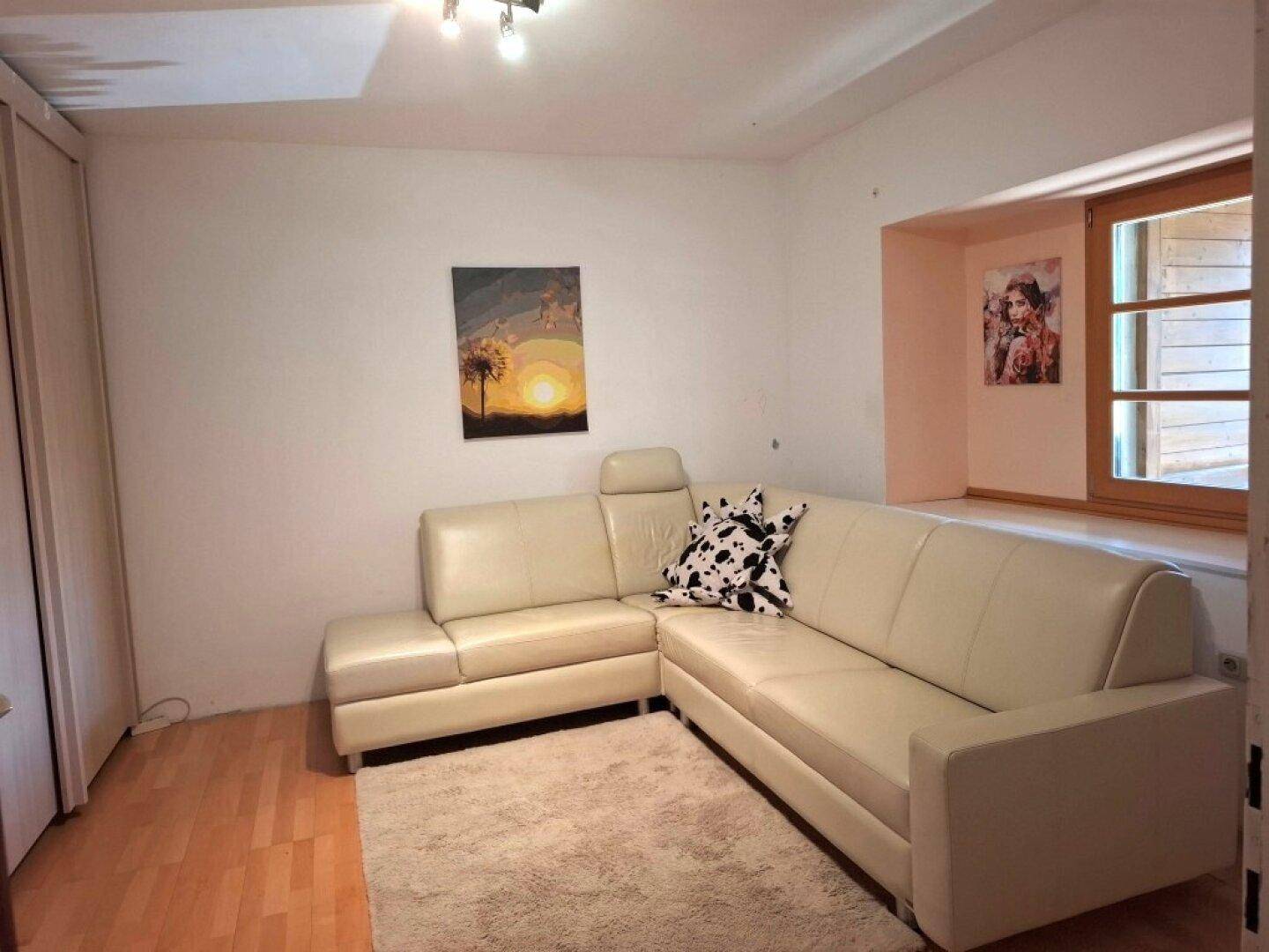 Gemütliches Wohnzimmer mit beigem Ecksofa, Teppich und einem Fenster mit Holzelementen.