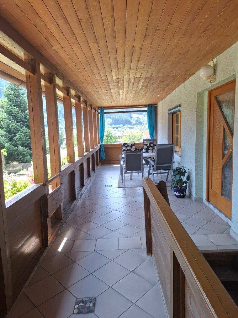 Überdachter Holzbalkon mit Fliesenboden und Sitzgelegenheiten, bietet einen Blick ins Grüne.